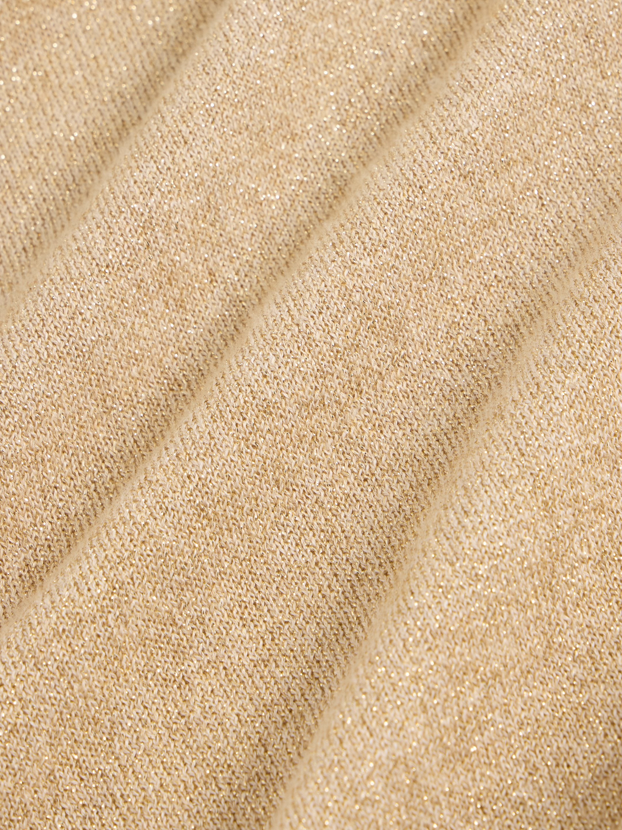Close-up of beige knit fabric with subtle gold glitter. The texture is soft and slightly draped.
