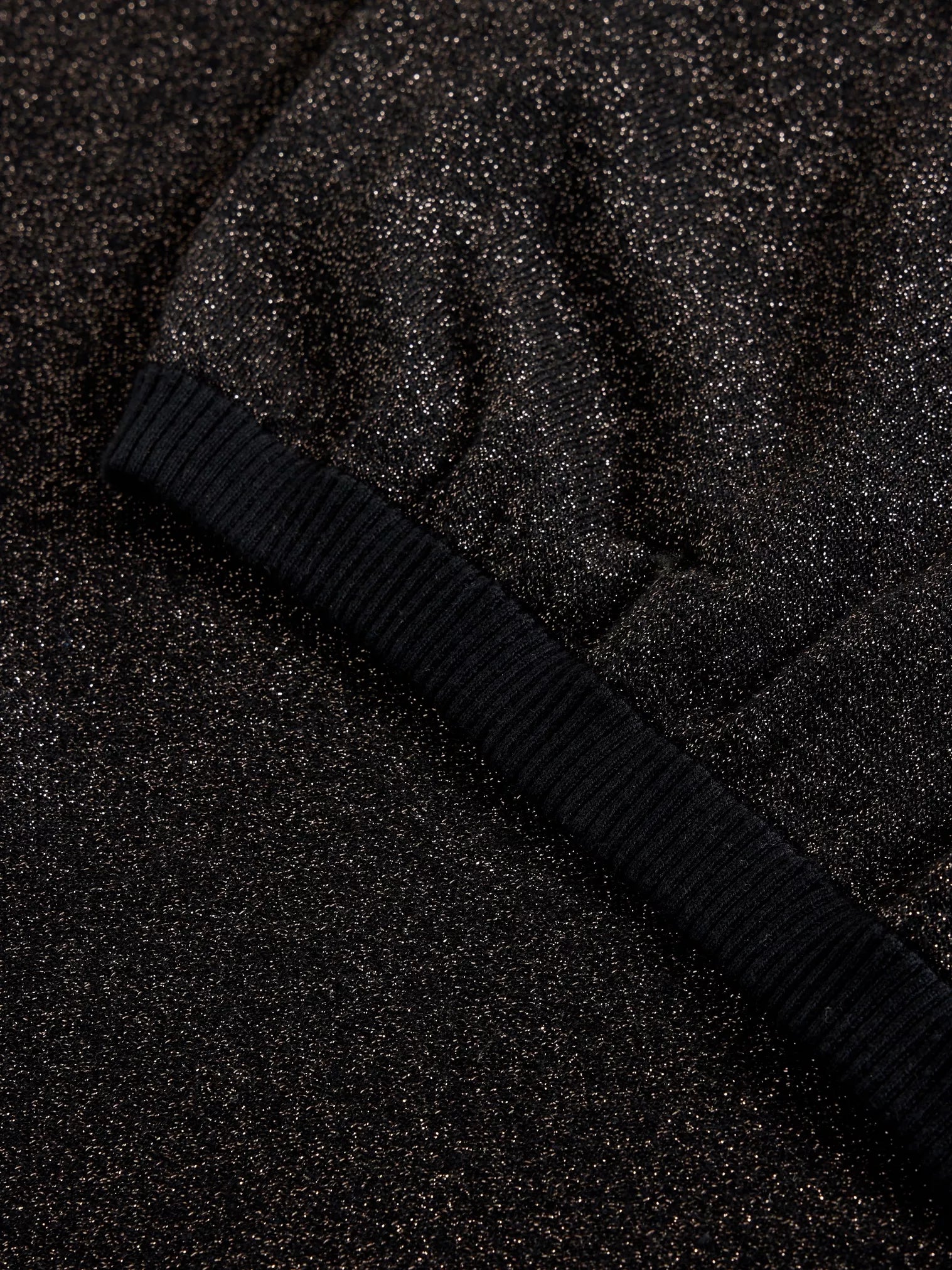Close-up of black glitter fabric with a black ribbed cuff.