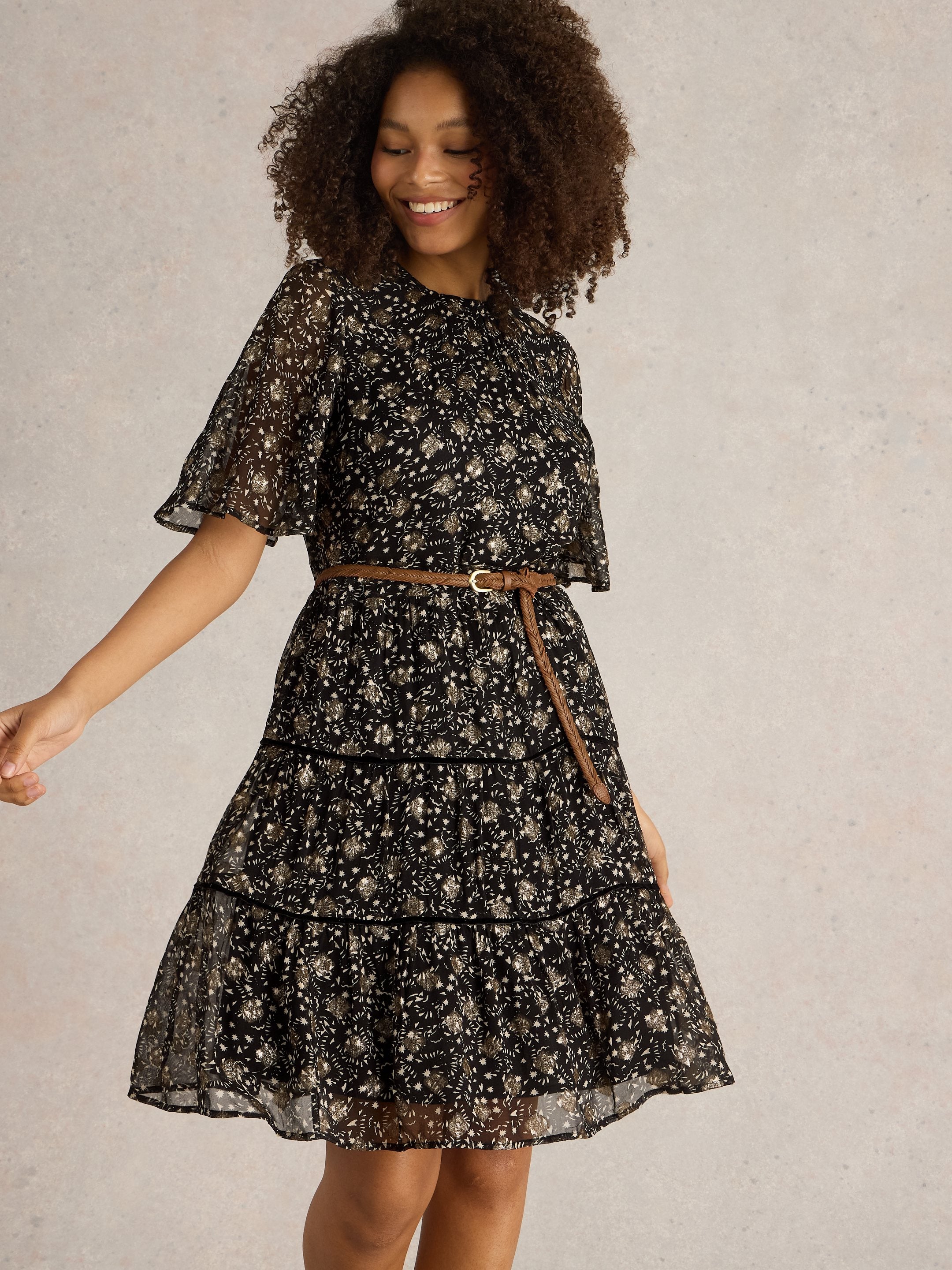 Black tiered mini dress with gold metallic floral print and short flutter sleeves. Brown braided belt included.