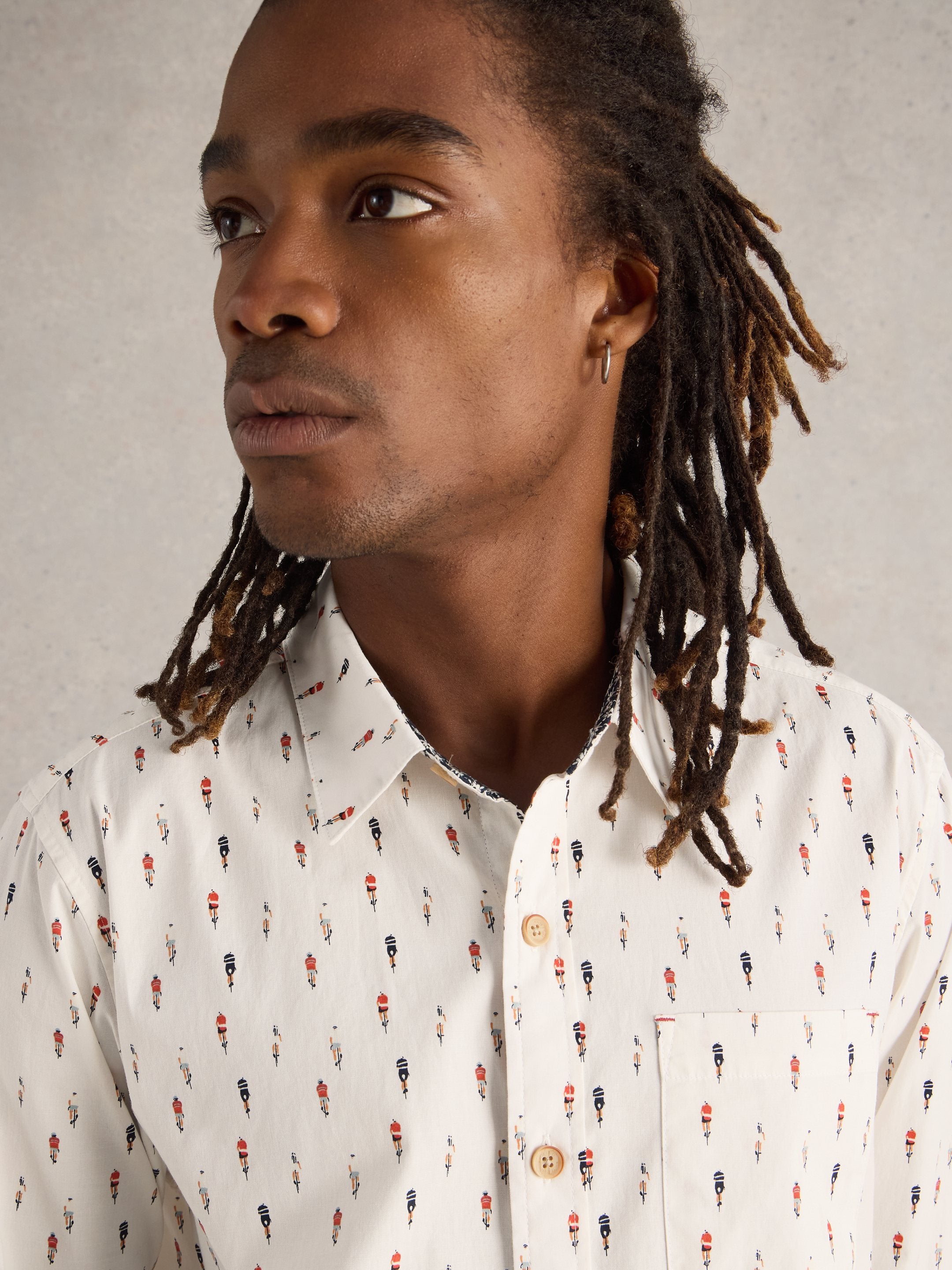Off-white short-sleeve button-down shirt with a repeating pattern of cyclists.