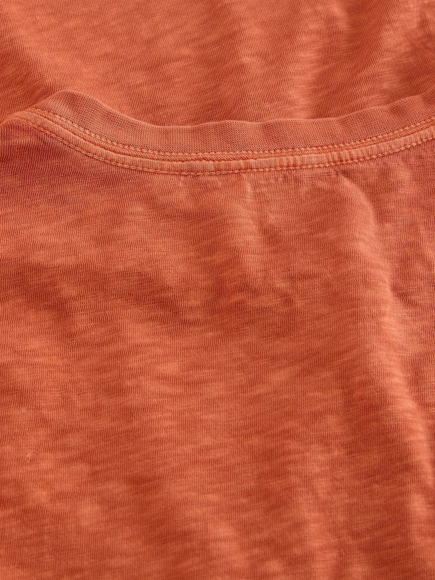 Close-up of rust-colored jersey knit fabric with a double-stitched neckline.