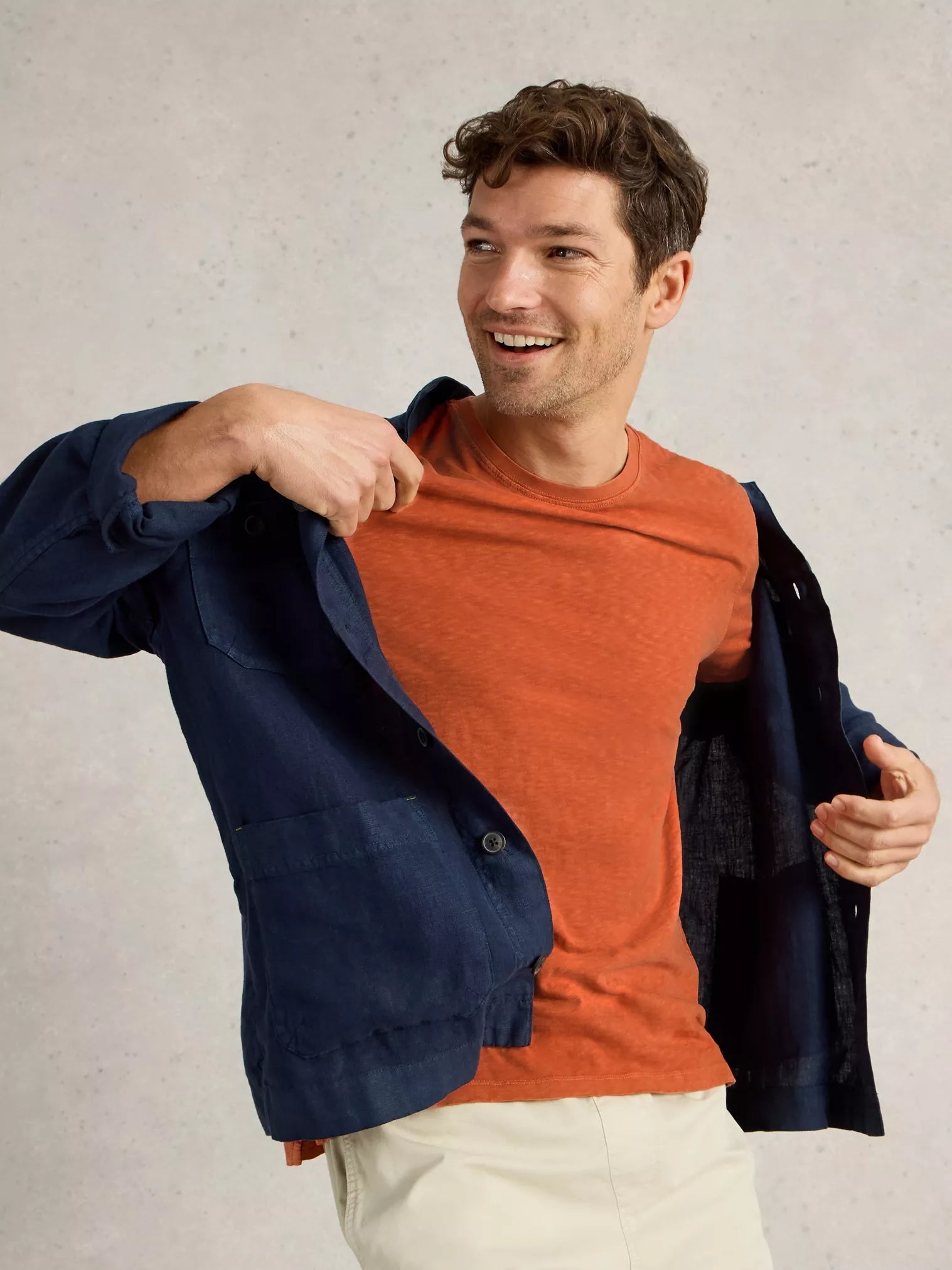 Man modeling a dark navy linen button-up jacket over an orange crew neck t-shirt and light beige pants.