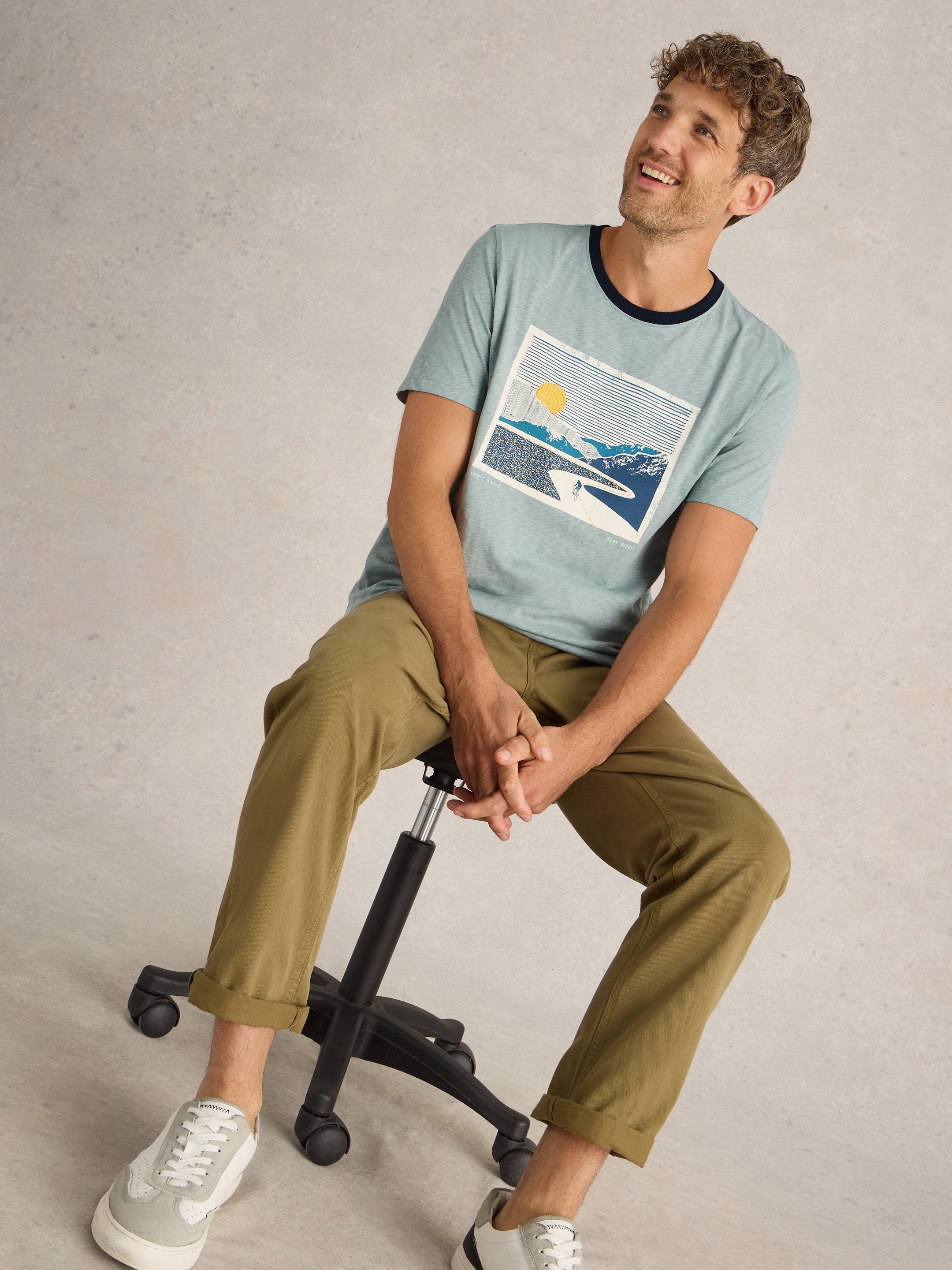 Light blue men's t-shirt featuring a graphic print of a sun, mountains, and a winding road.