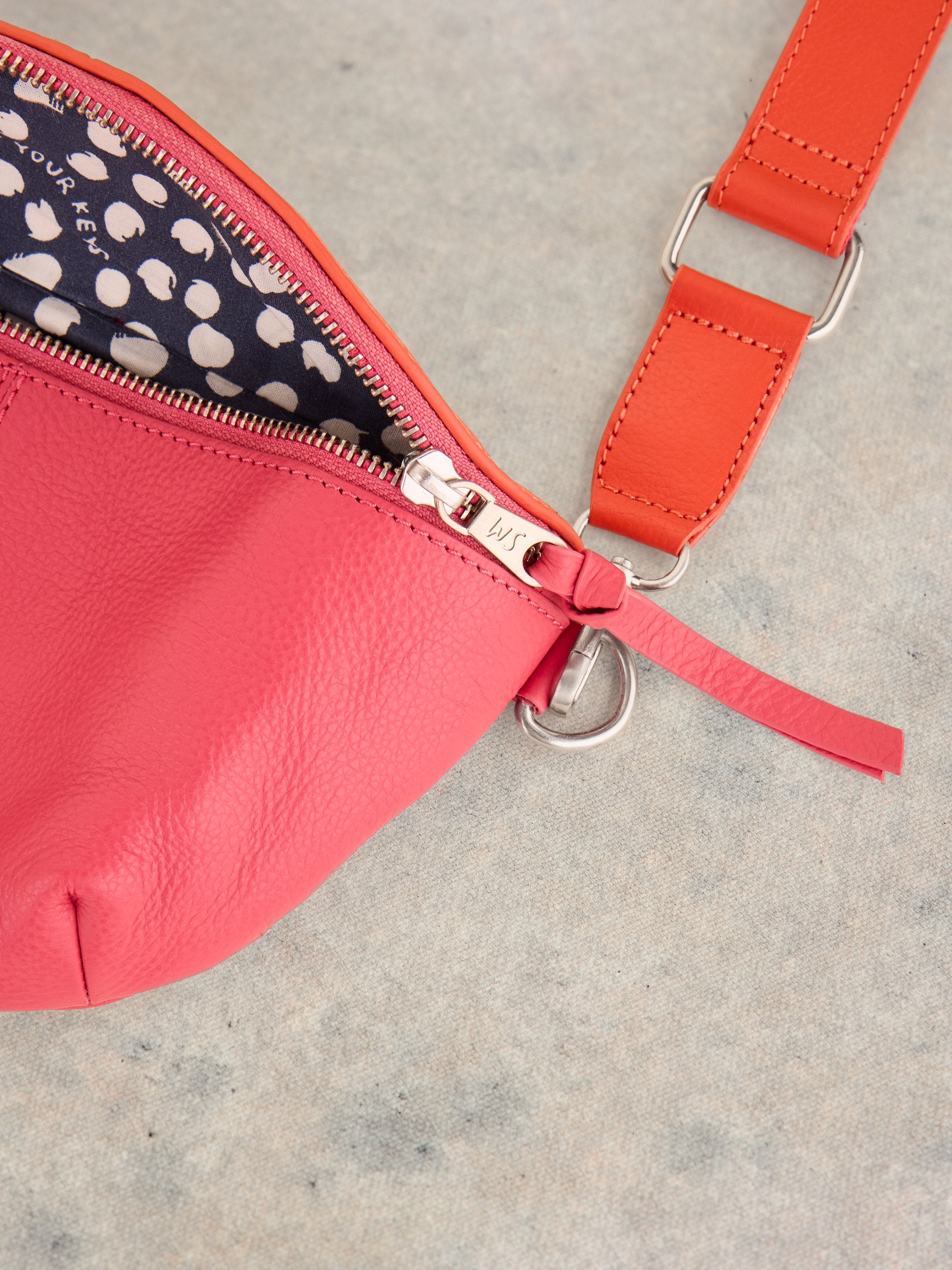 Pink leather crossbody bag with orange strap and silver zipper.