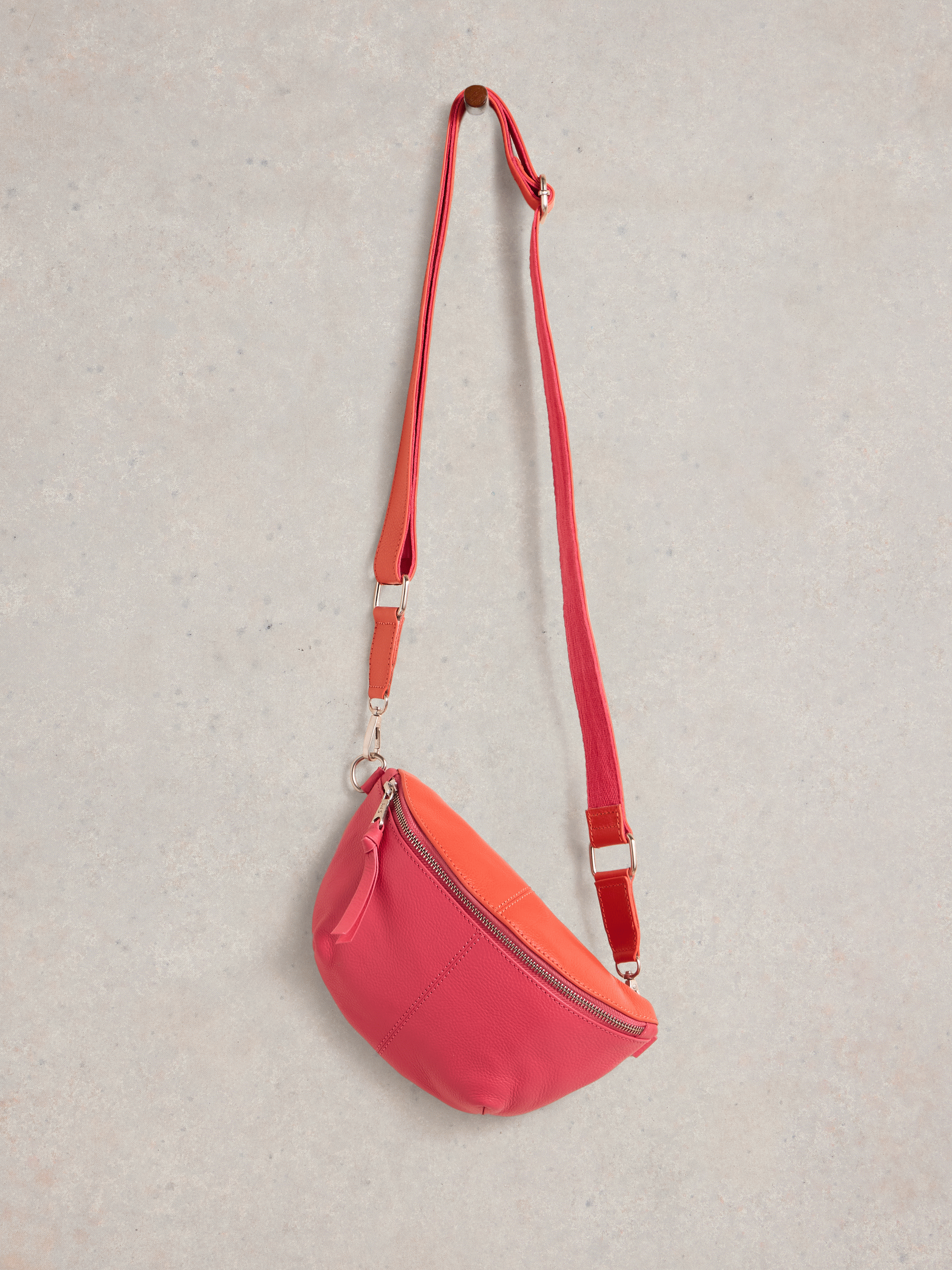 Pink leather fanny pack with a long adjustable strap and silver zipper.