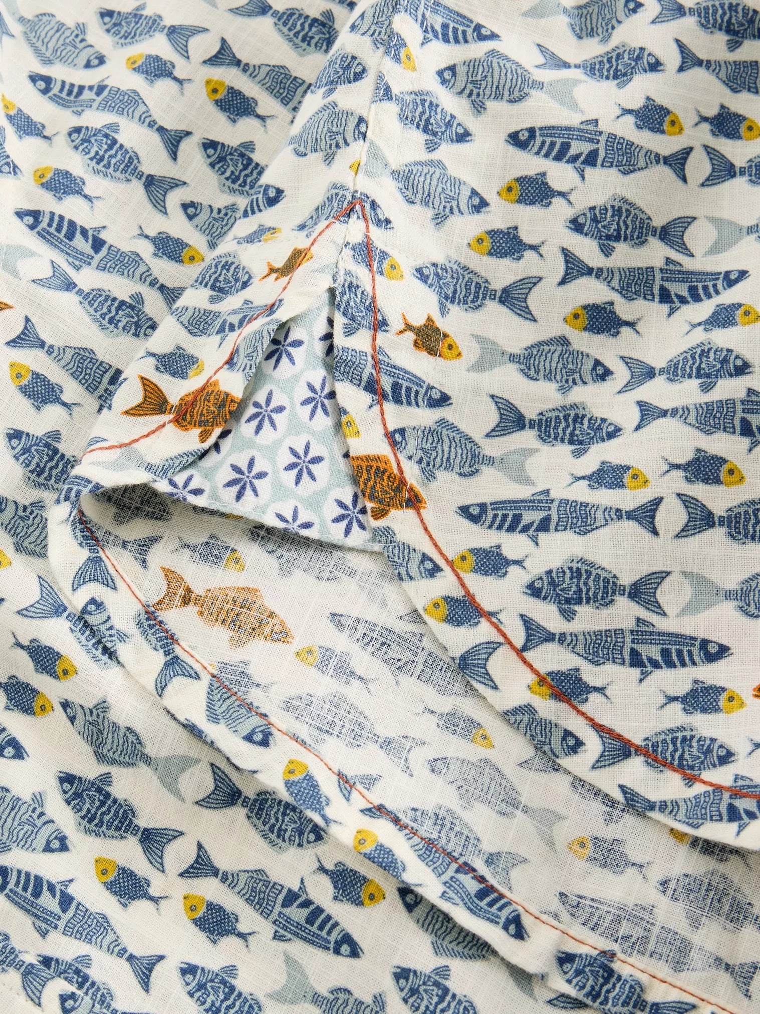 Off-white fabric with a repeating pattern of blue and orange stylized fish. The fabric shows a seam detail.