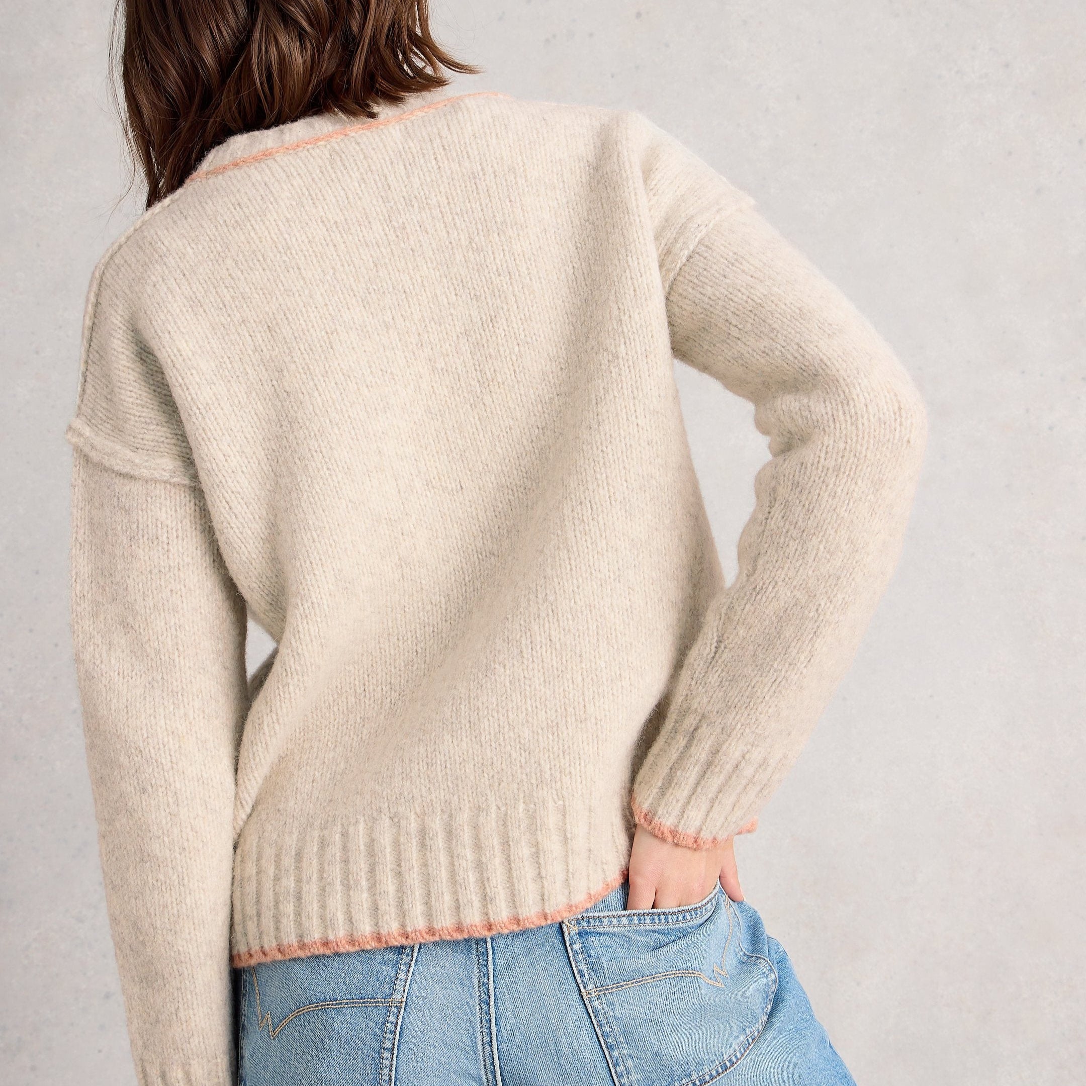 Person wearing a beige sweater and blue jeans against a plain background