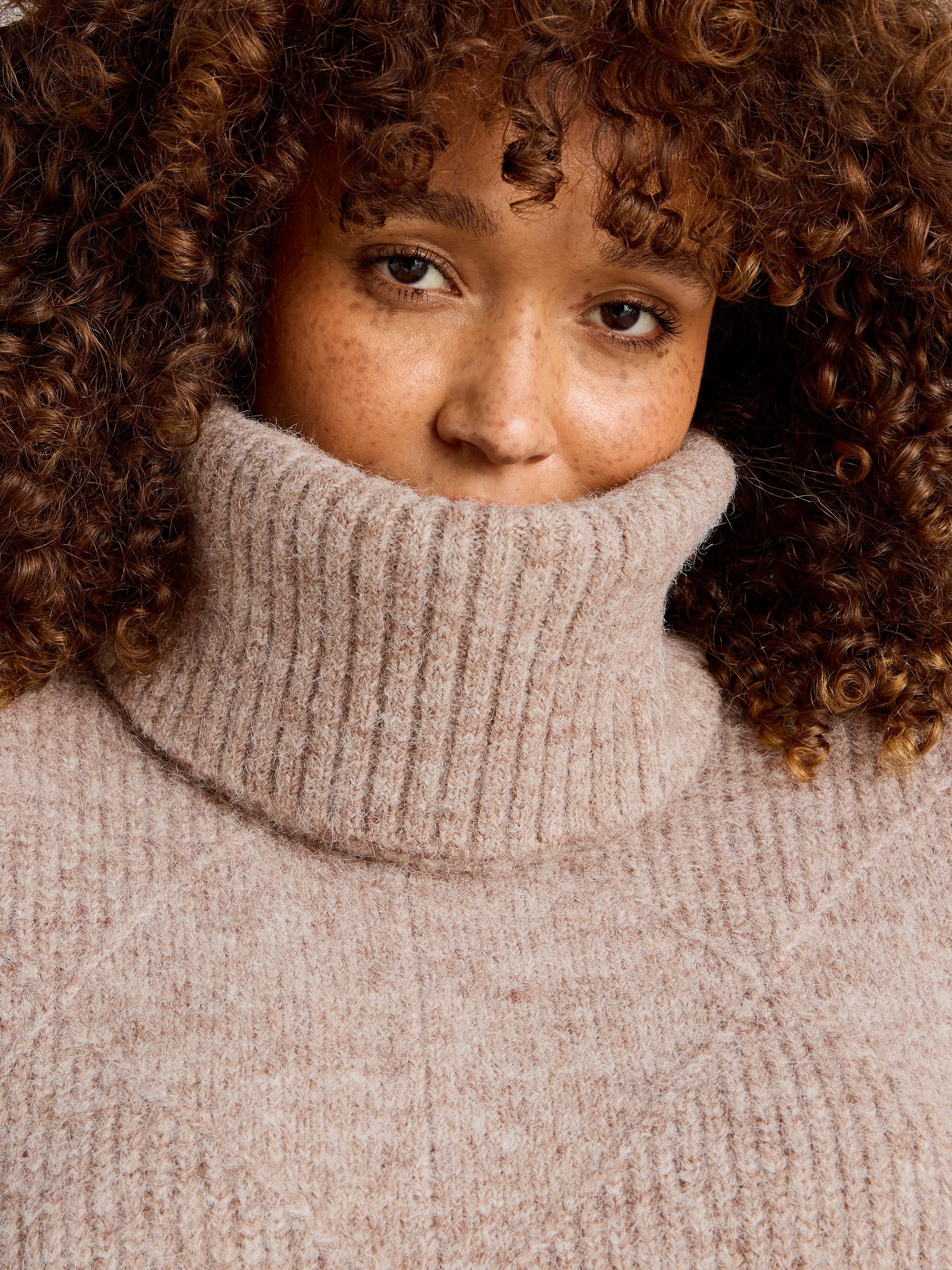 Person wearing a beige turtleneck sweater with curly hair