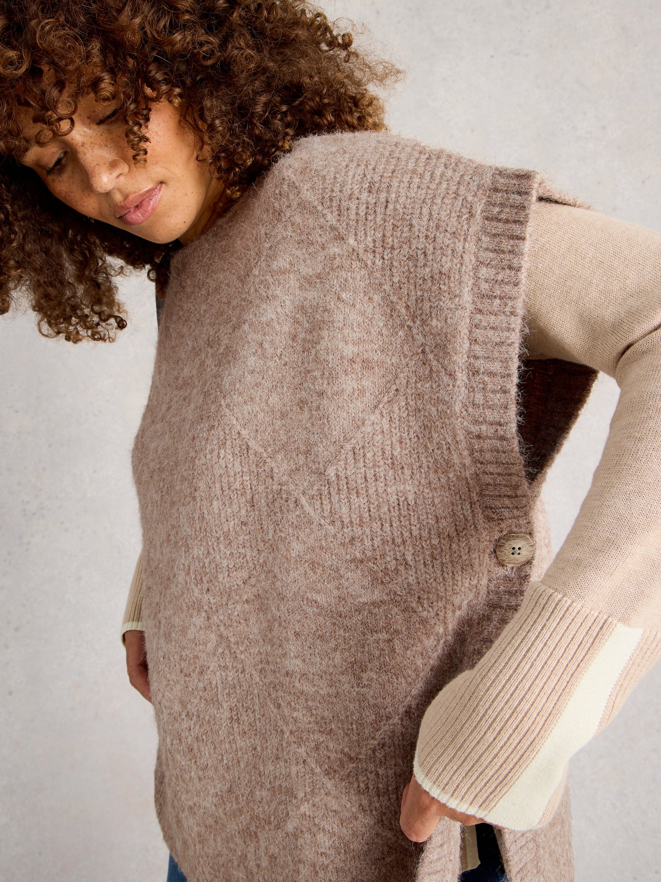 Person wearing a brown knitted vest against a neutral background