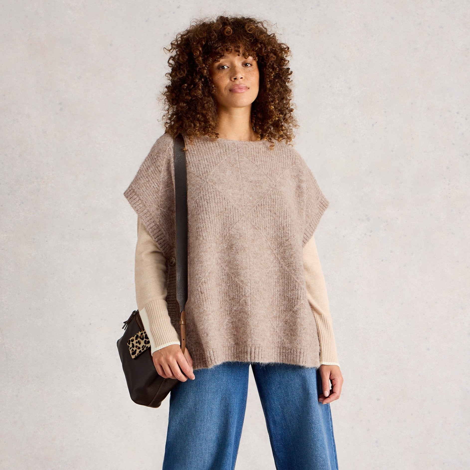 Woman wearing a beige poncho and blue jeans against a plain background