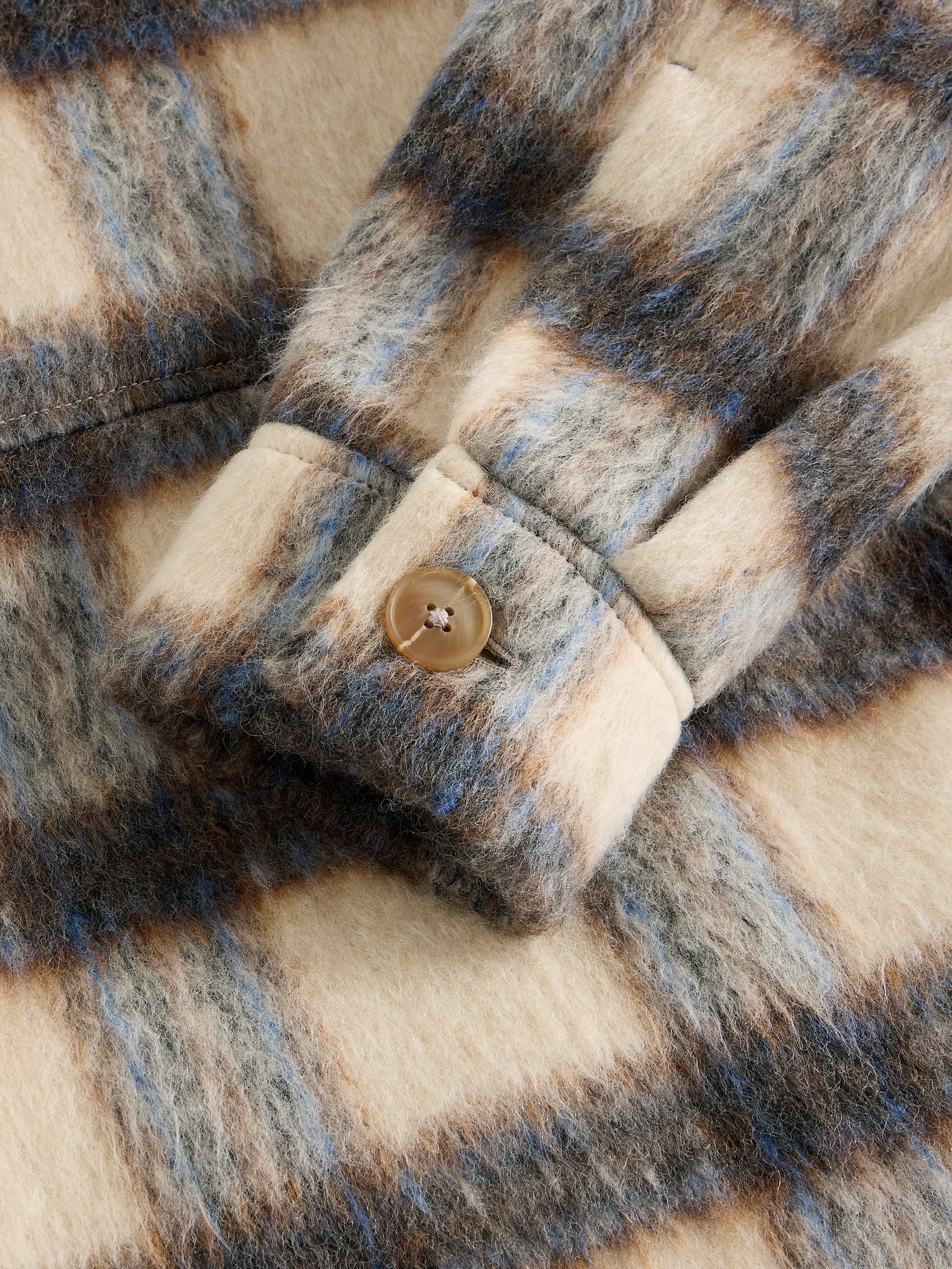 Close-up of a plaid fabric with a button, showing texture and pattern details.