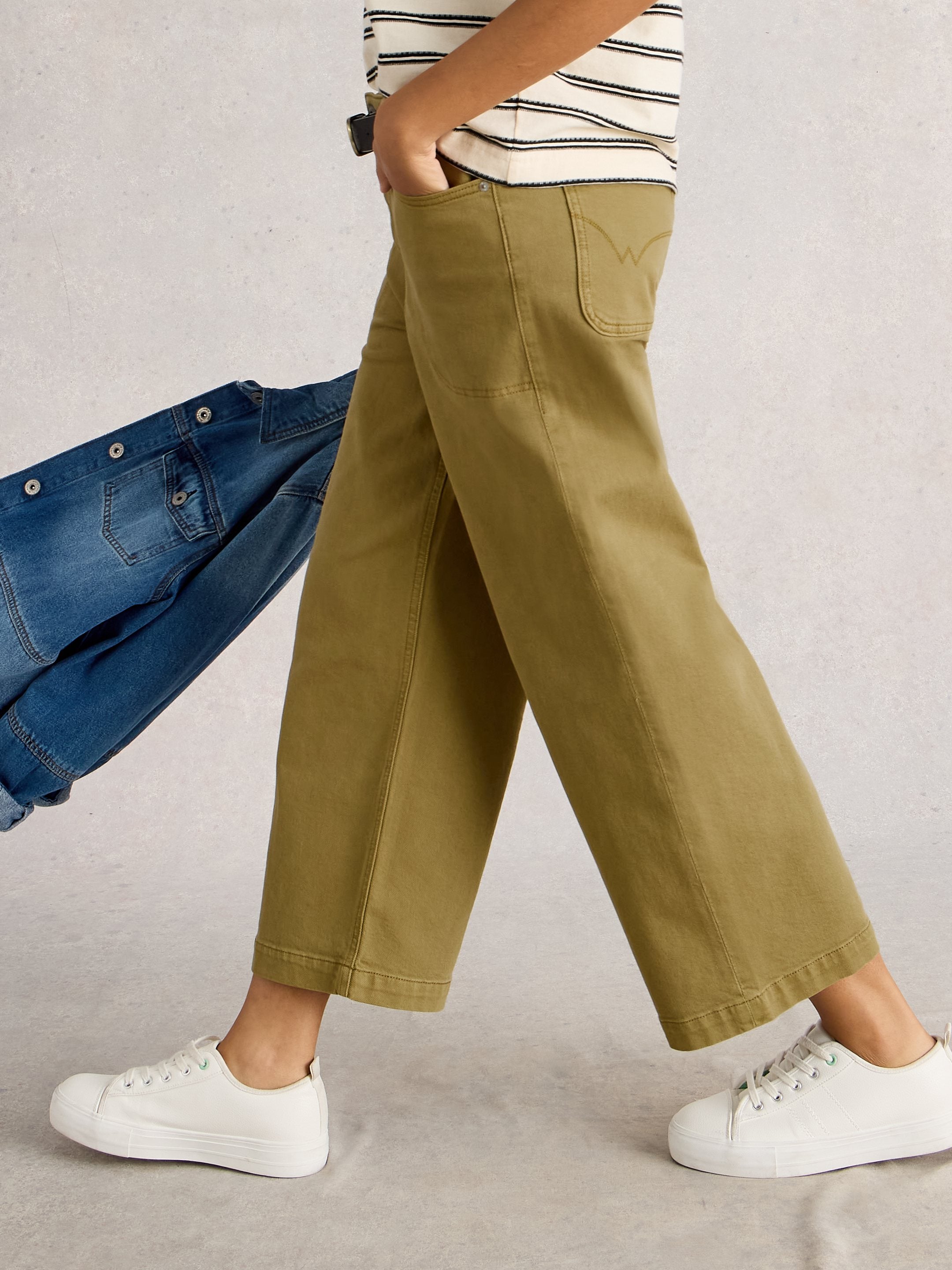 Person wearing green pants and white sneakers with a blue denim jacket on a light gray background