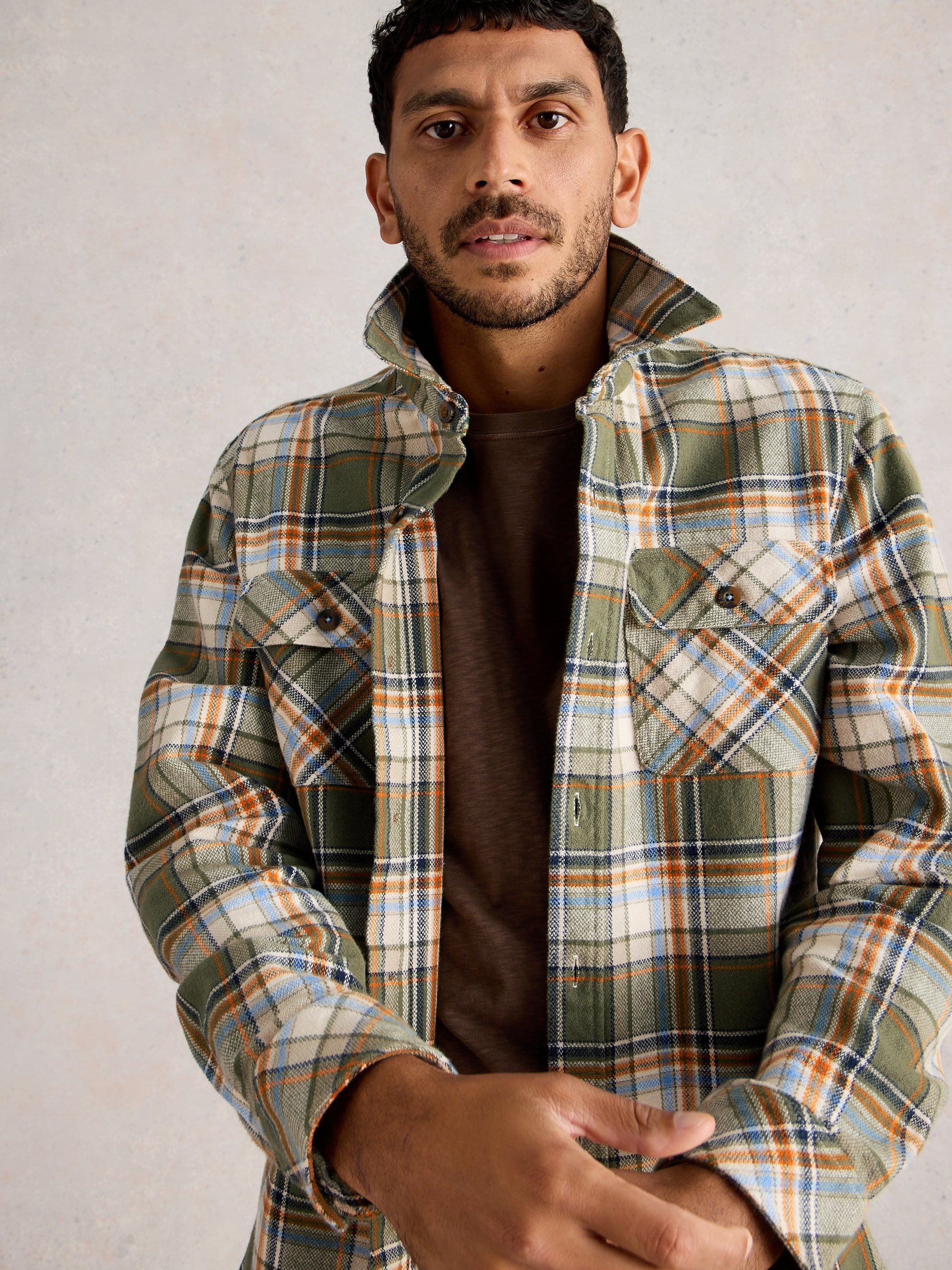 Man wearing a plaid jacket over a brown shirt against a plain background
