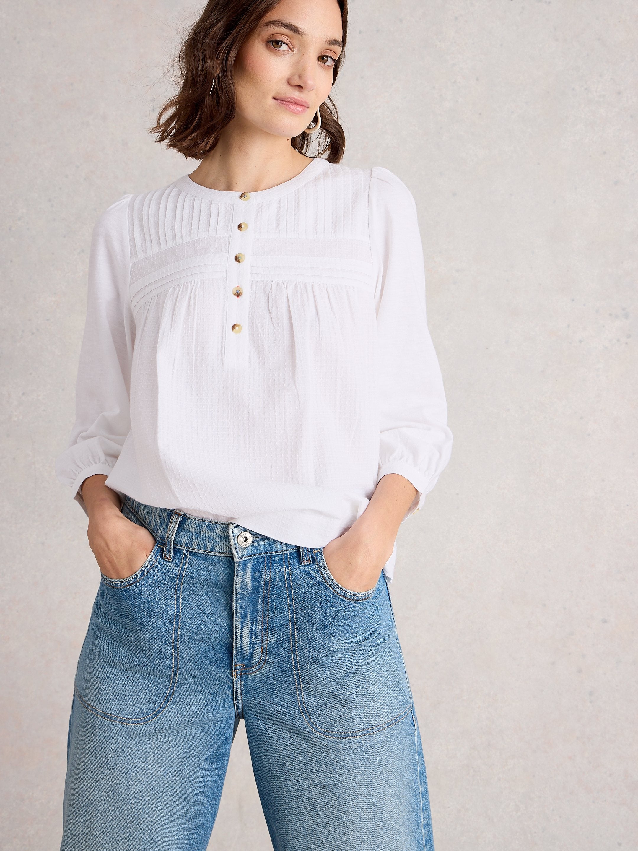 Woman wearing a white blouse and blue jeans against a plain background