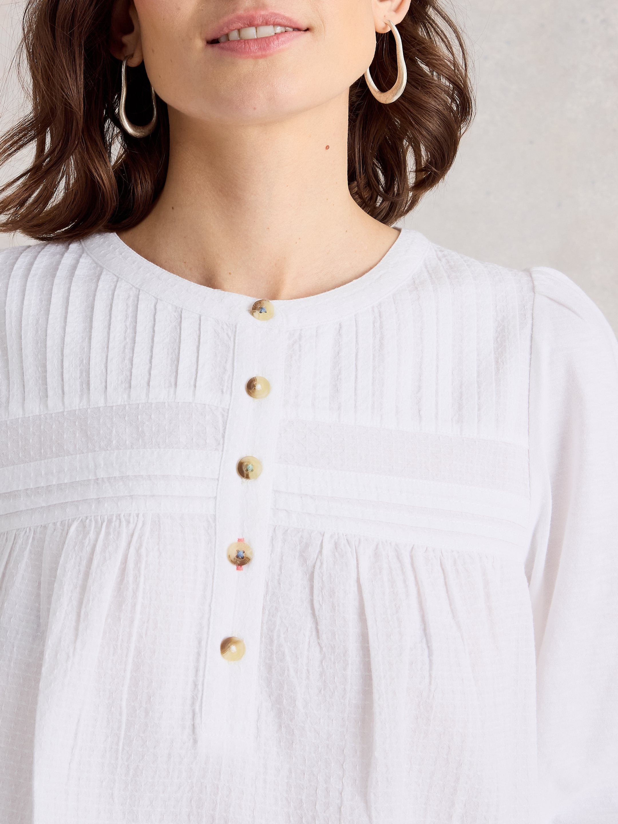 White blouse with gold buttons worn by a person, on a neutral background