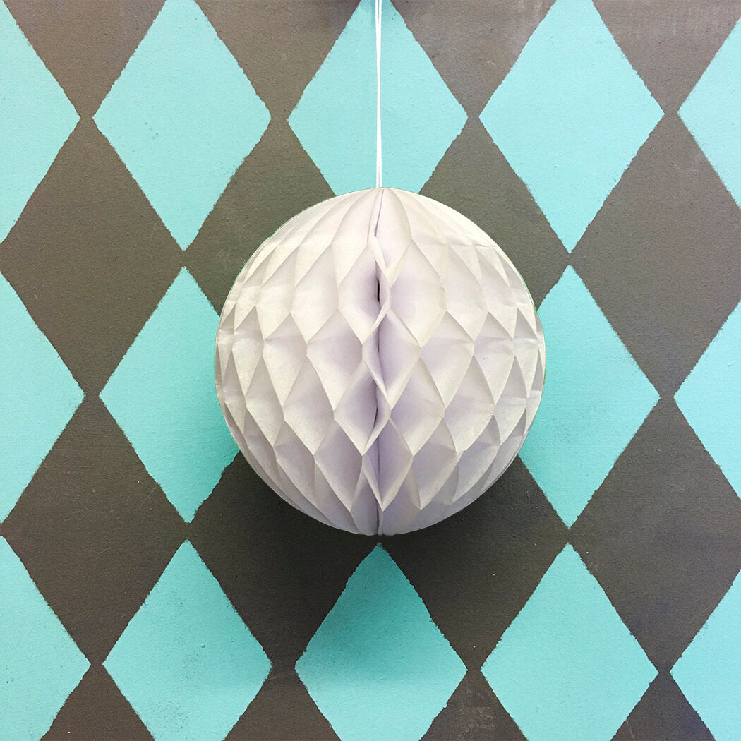 Off-white honeycomb paper ball decoration hanging against a teal and brown diamond patterned background.