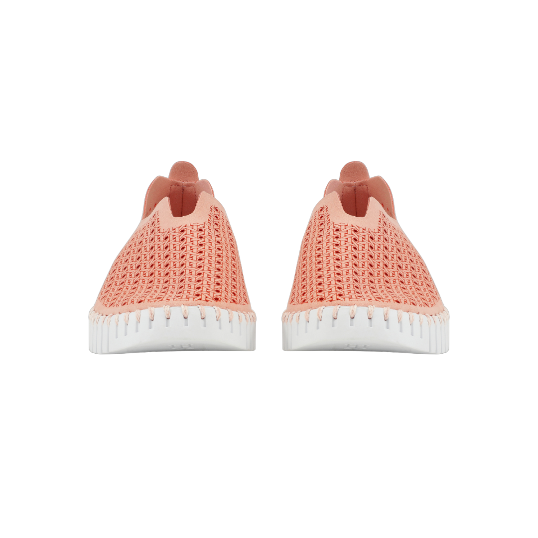 Pair of coral woven slip-on sneakers with white soles. The shoes feature a textured, breathable upper and a slightly scalloped