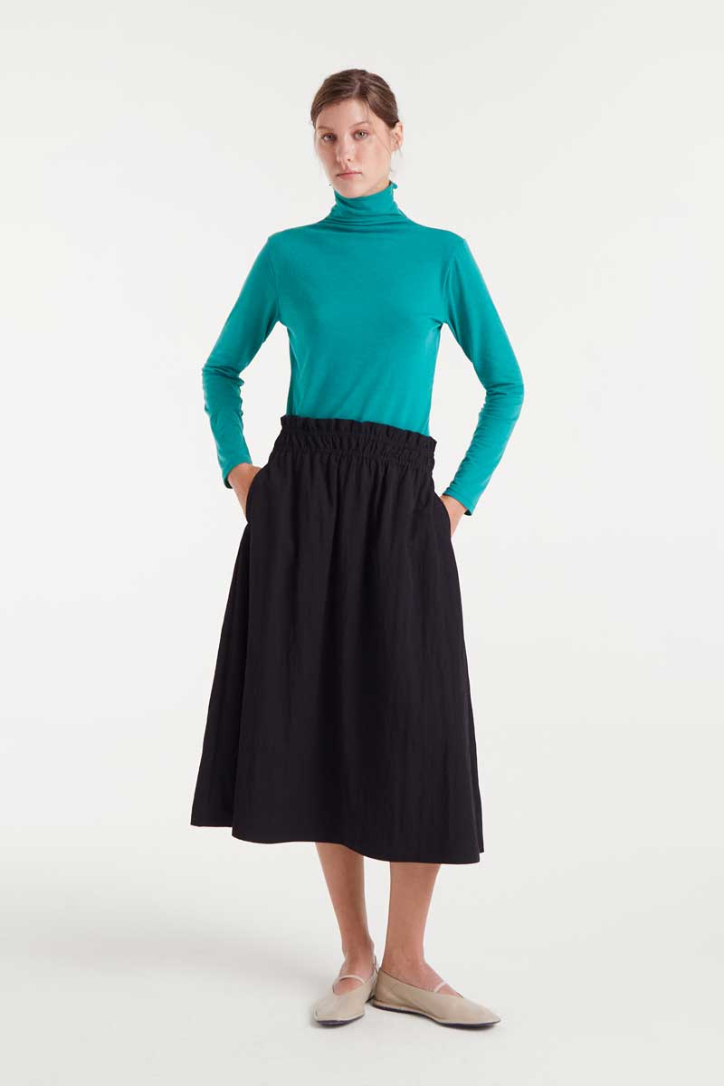 Woman wearing a turquoise turtleneck and black skirt on a white background