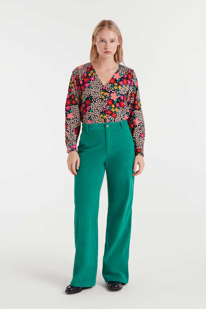 Woman wearing a colorful floral blouse and green pants on a white background