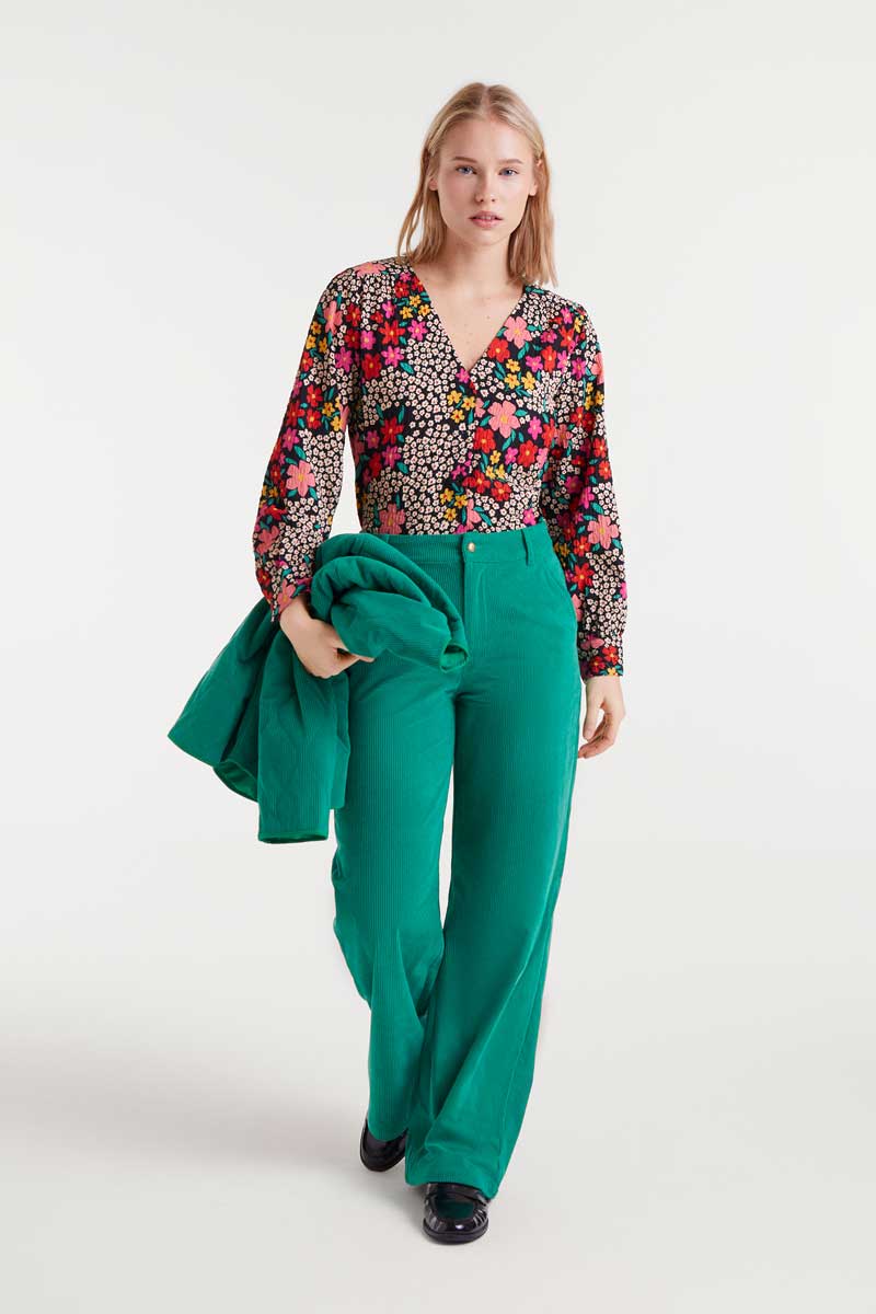 Woman wearing a floral top and green pants on a white background