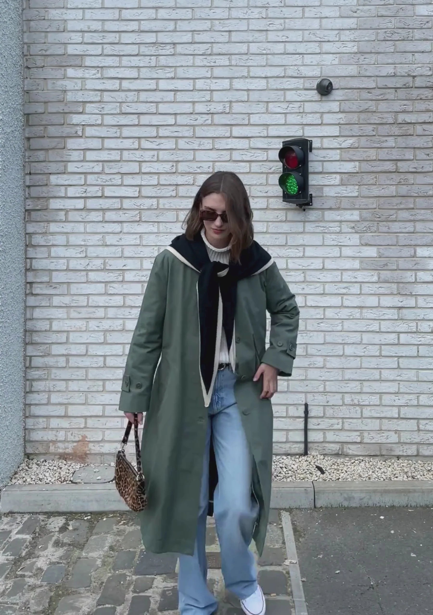 A long, olive-green trench coat with a black and cream scarf.