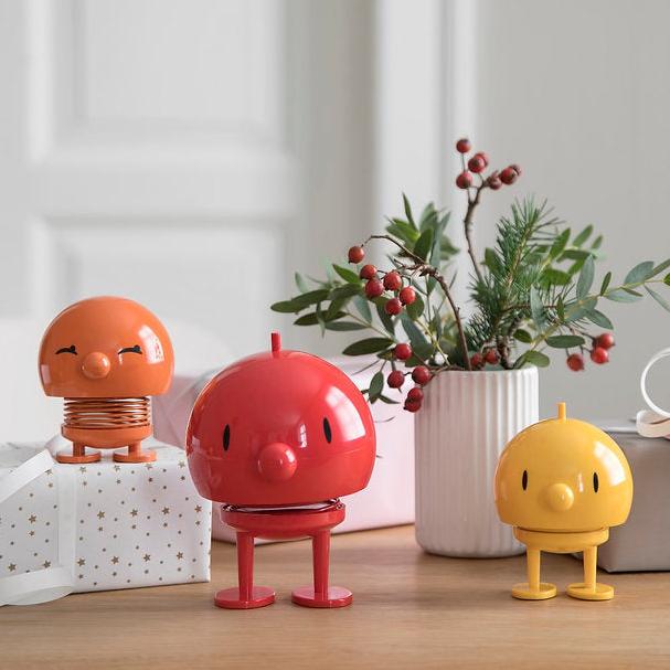 Three bobblehead-style figures; orange, red, and yellow; each with a smiling face and short legs.