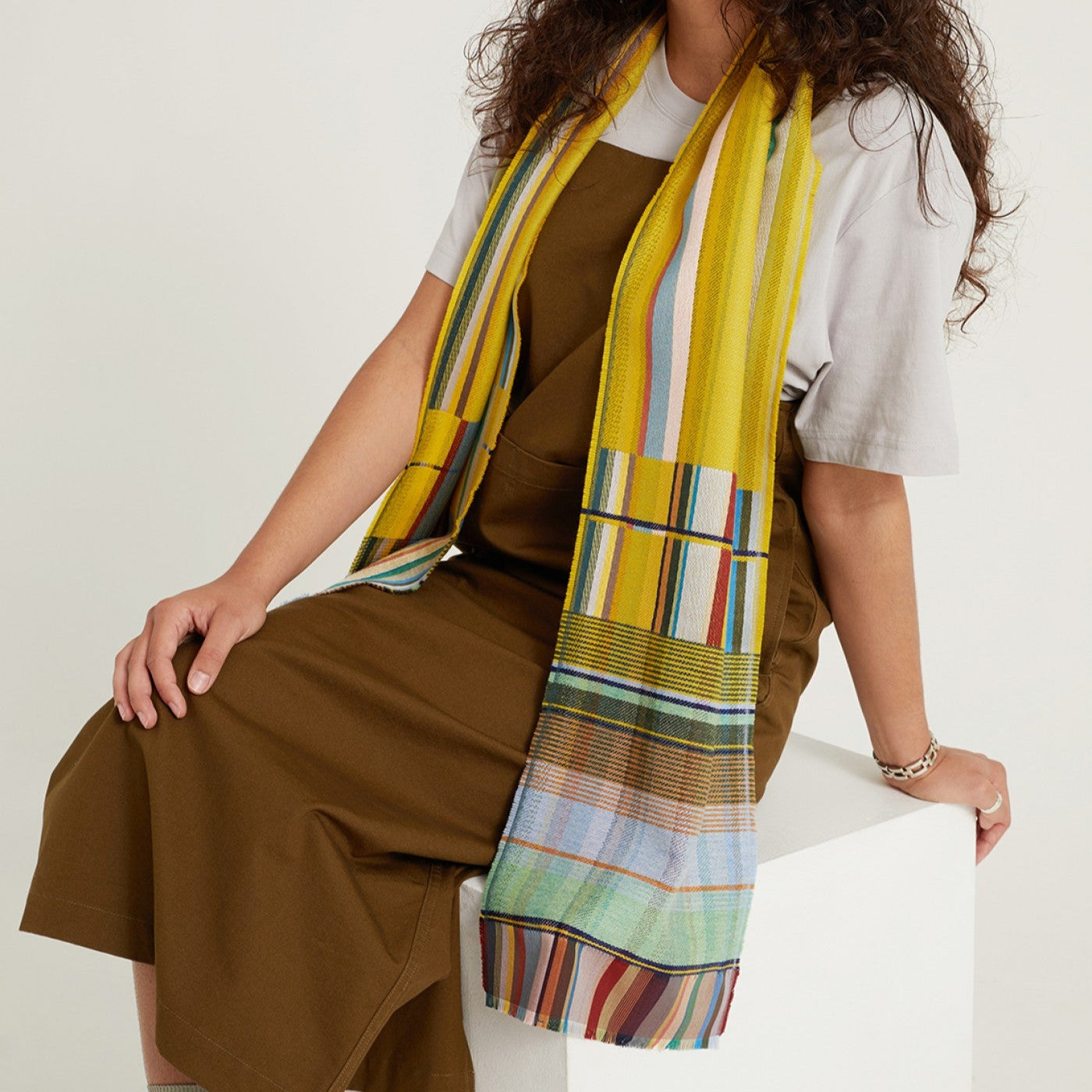 Multicolored striped and plaid woven scarf in predominantly yellow and muted greens, blues, and browns.