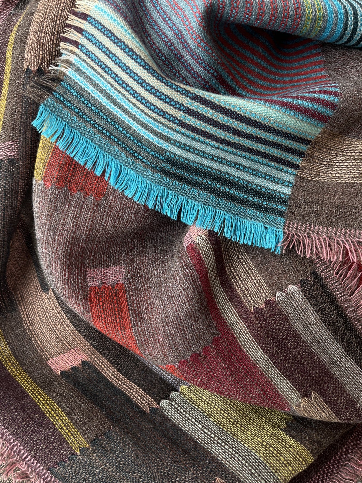 Woven shawl with multicolored stripes and geometric patterns in shades of brown, teal, red, and pink.