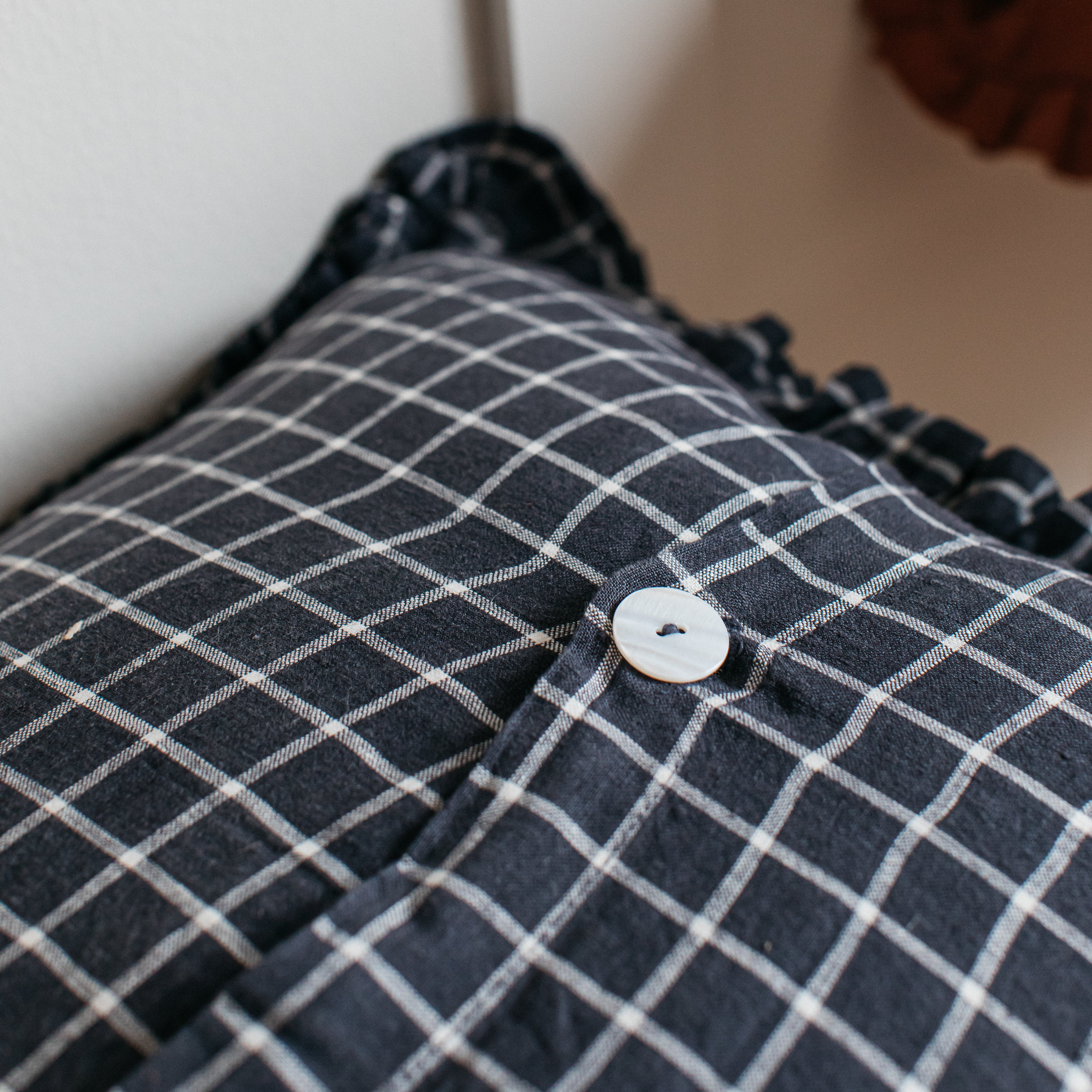 Close-up of a dark gray and white gingham pillow with ruffled edges and a large off-white button.