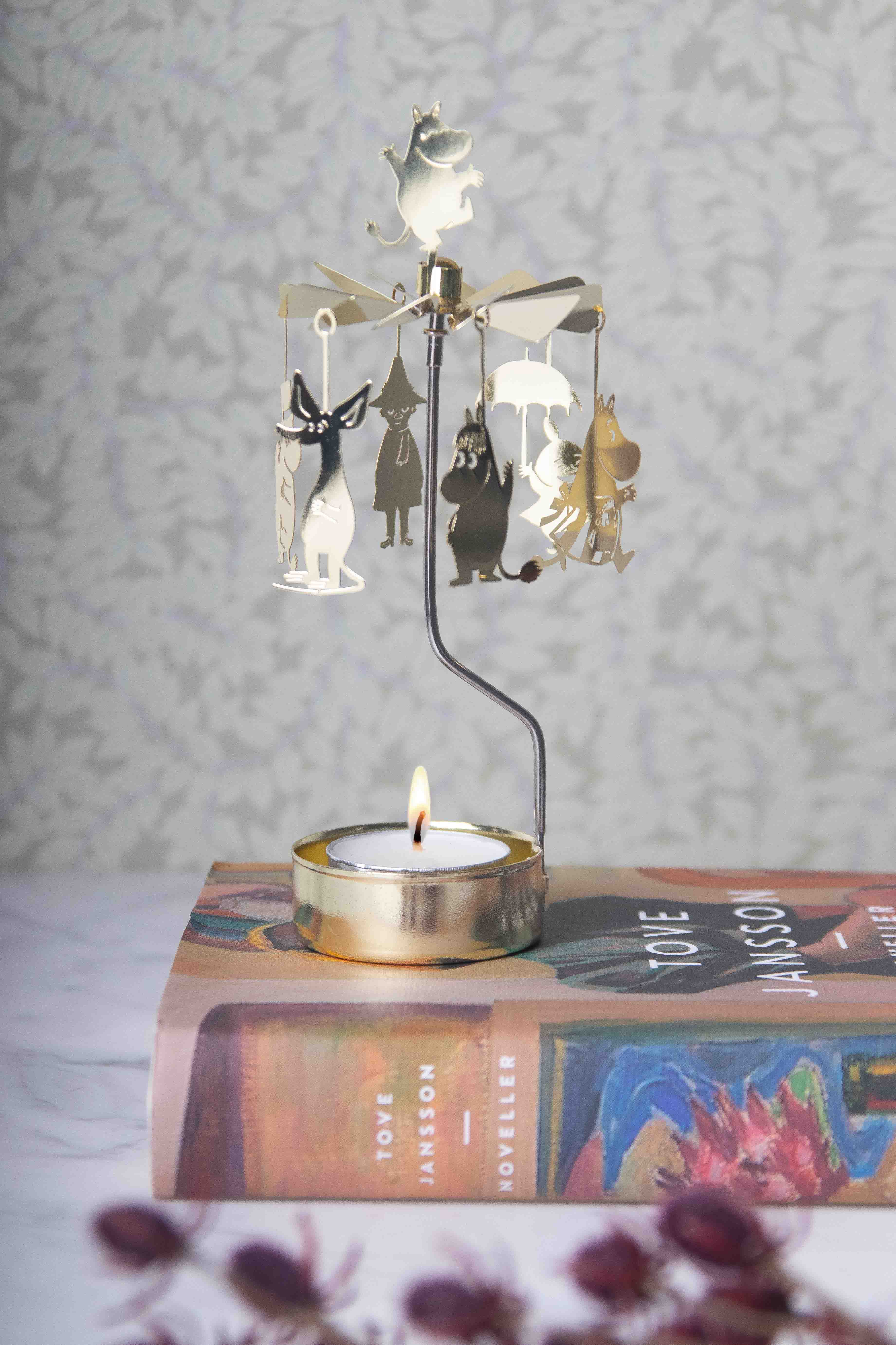 Gold Moomin-themed candleholder with a spinning carousel featuring Moomin characters. A lit tea light candle sits below.