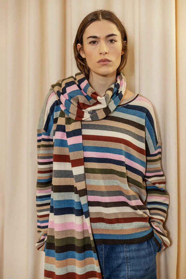 Person wearing a multicolored striped sweater against a beige curtain background