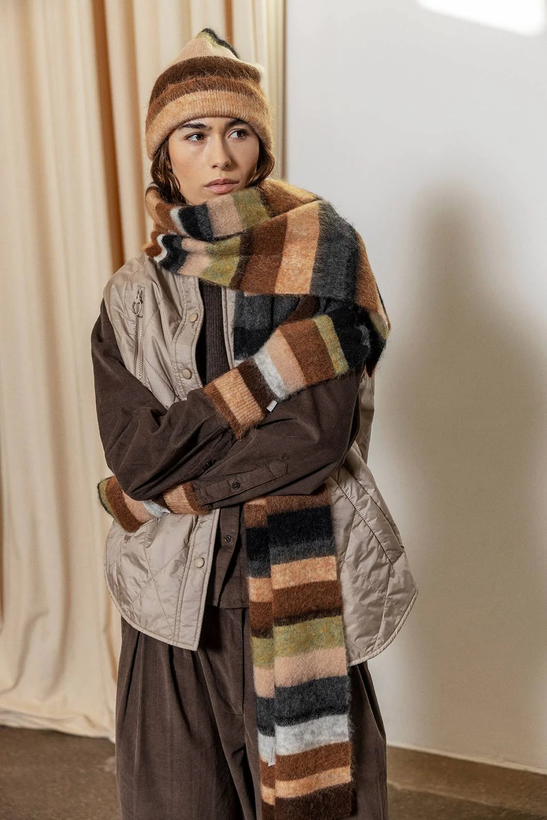 Person wearing a striped scarf and hat in a neutral setting