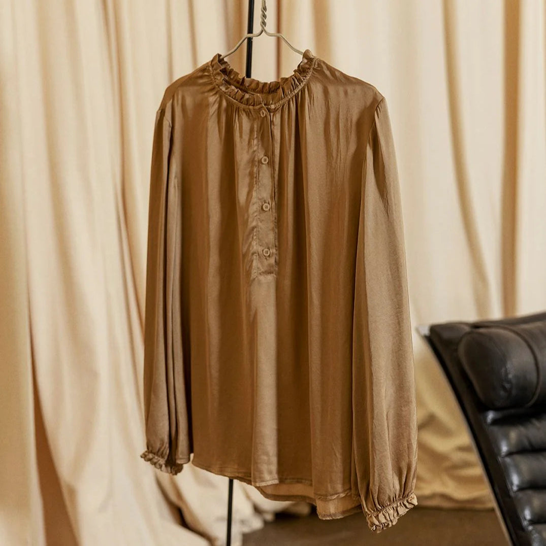 Brown blouse on a hanger against a beige curtain background