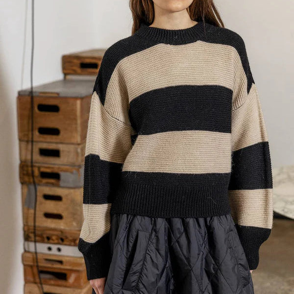 Woman wearing a black and beige striped sweater with a dark quilted skirt in an indoor setting.
