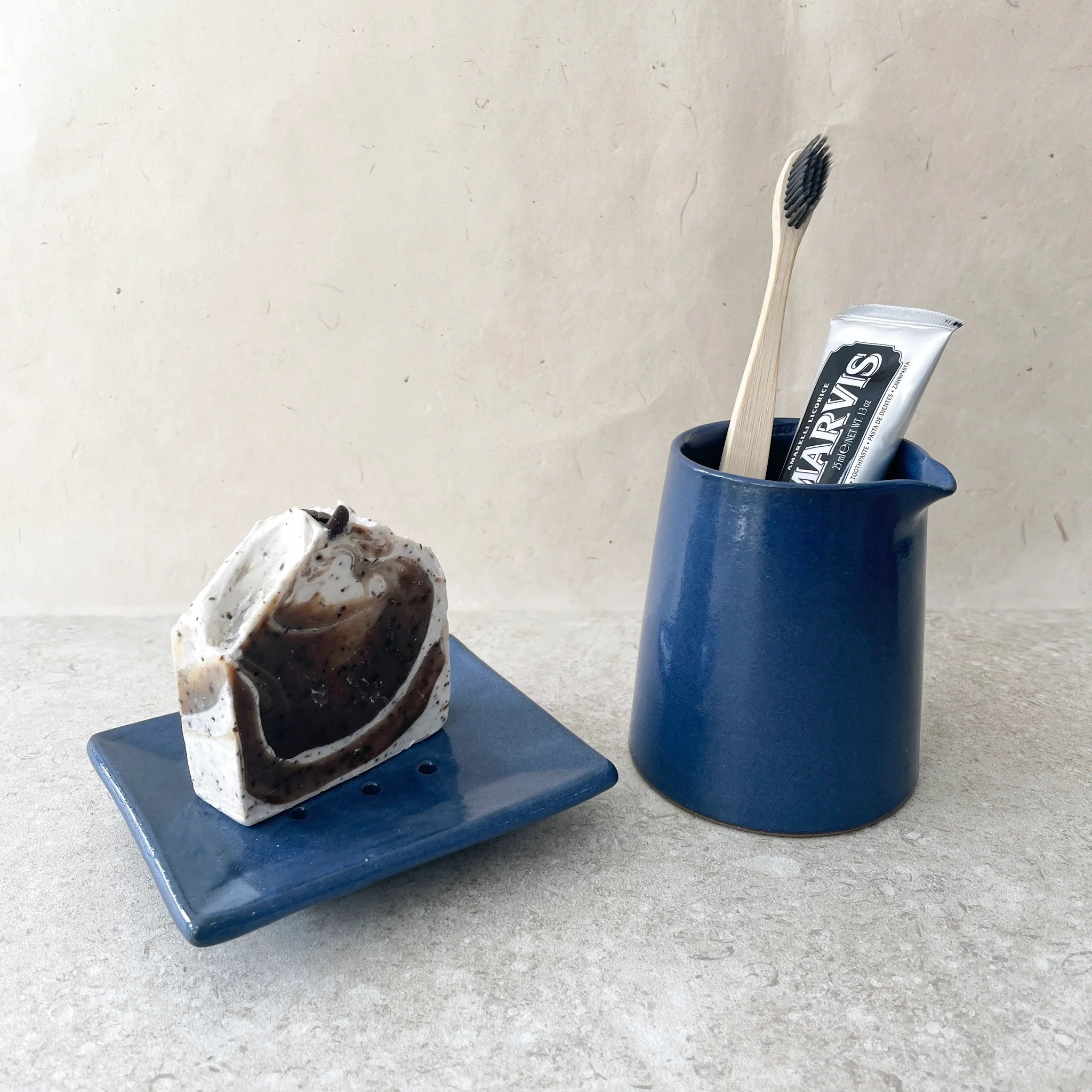 Dark brown and cream marbled soap on a blue ceramic dish, next to a blue ceramic holder with a bamboo toothbrush and tube of