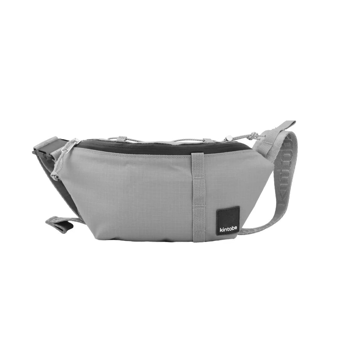 Grey fabric fanny pack with black accents and adjustable straps. Features a small brand label.