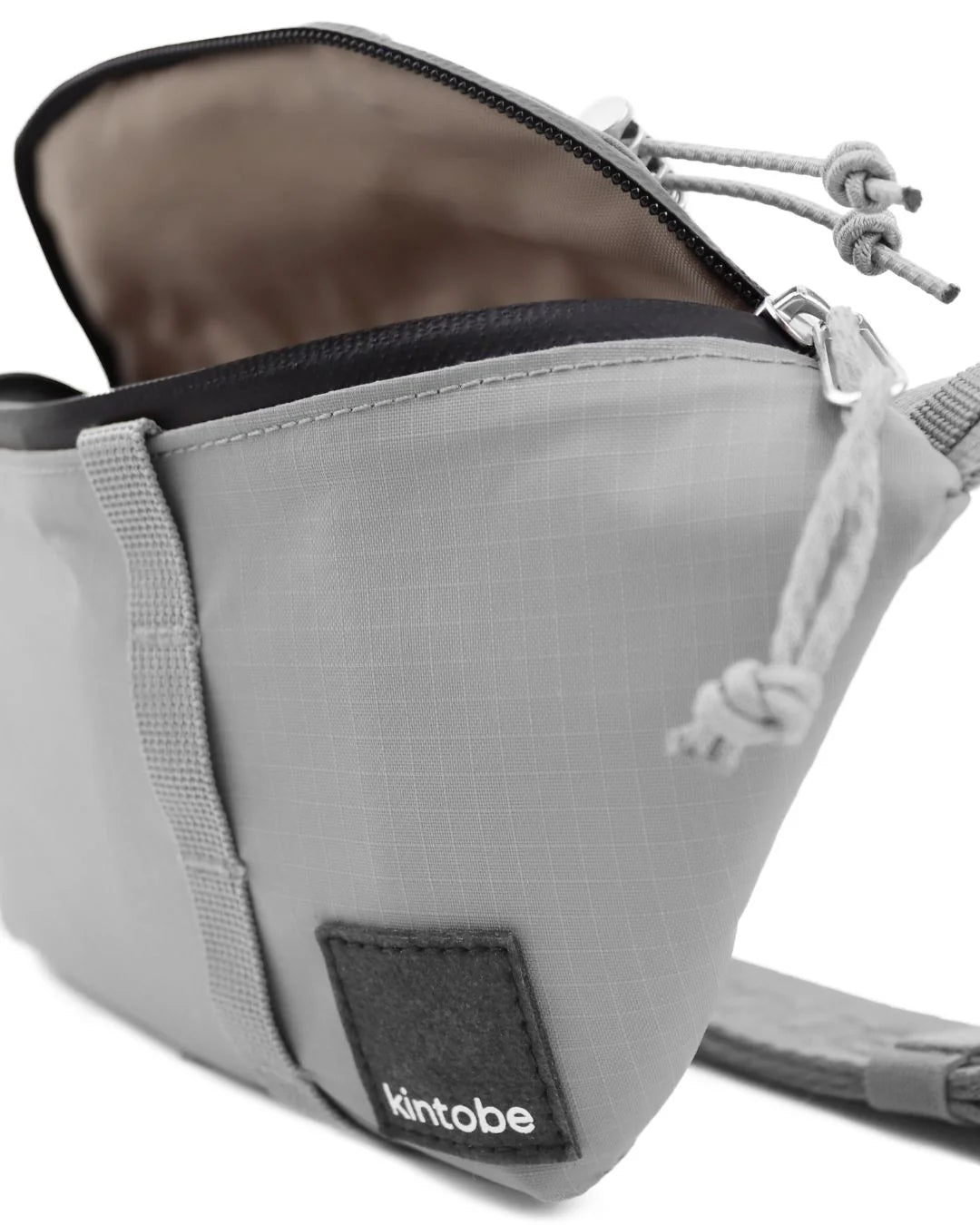 Light gray Kintobe fanny pack with black zipper and adjustable strap. The pack is partially open, showing its interior.