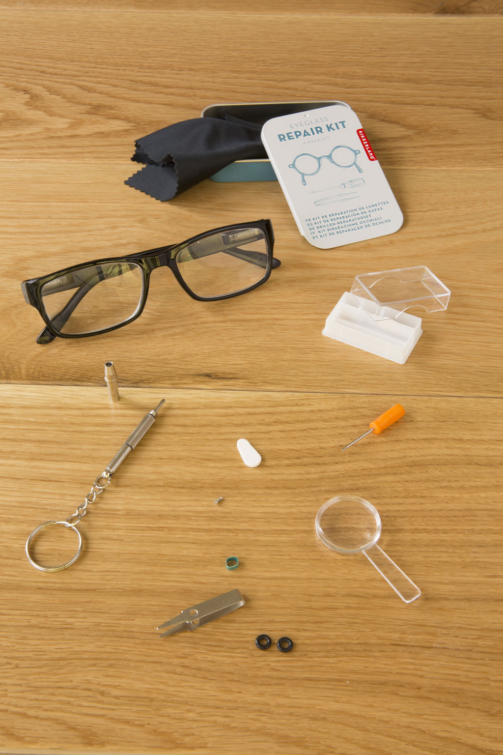 Eyeglass repair kit with tools, a cleaning cloth, and replacement parts in a tin.