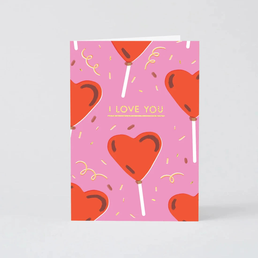 Pink greeting card featuring a repeating pattern of red heart-shaped lollipops, gold confetti, and the text "I LOVE YOU."