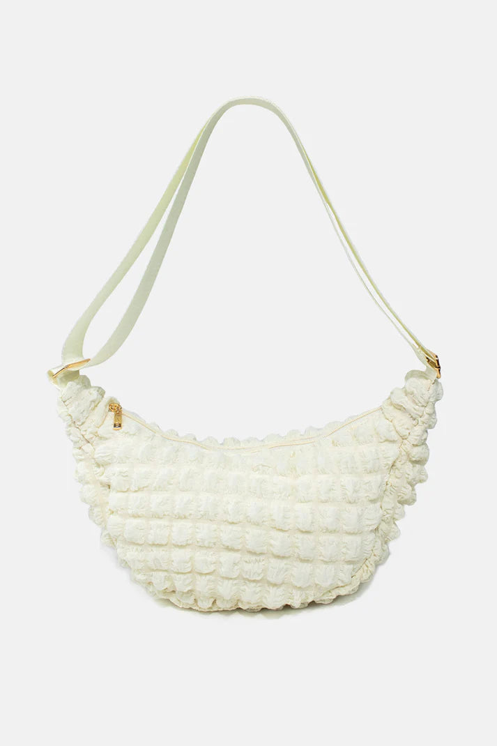 Off-white textured crossbody bag with a crescent shape and light-colored straps.