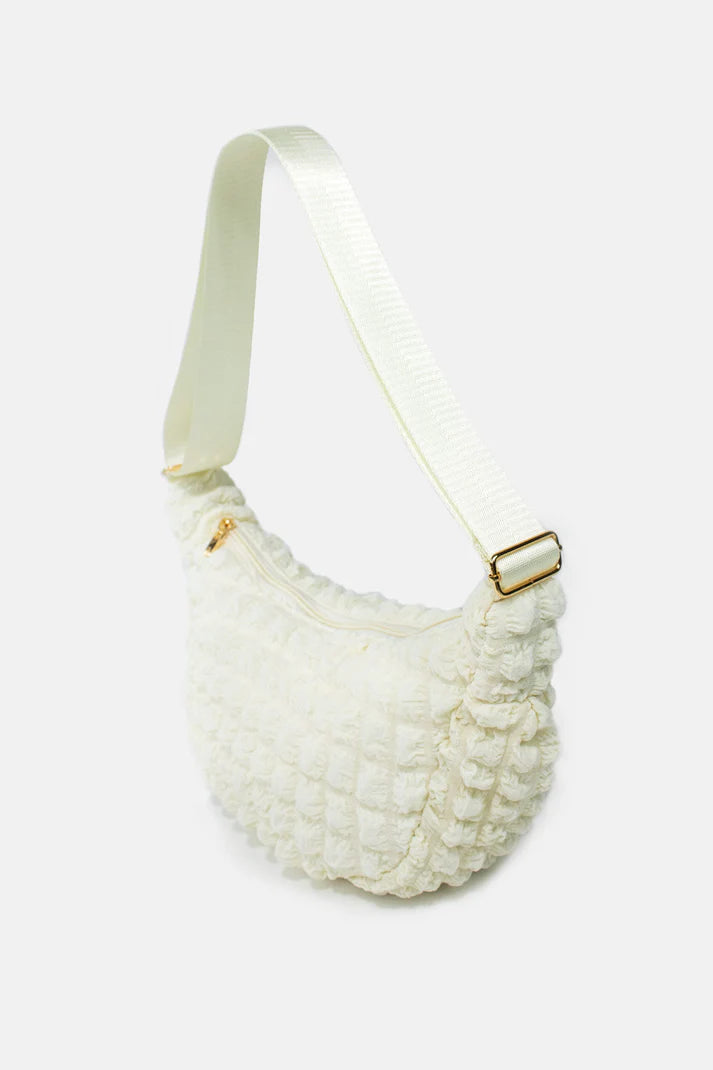 Off-white textured fabric half-moon crossbody bag with a light beige adjustable strap and gold zipper.