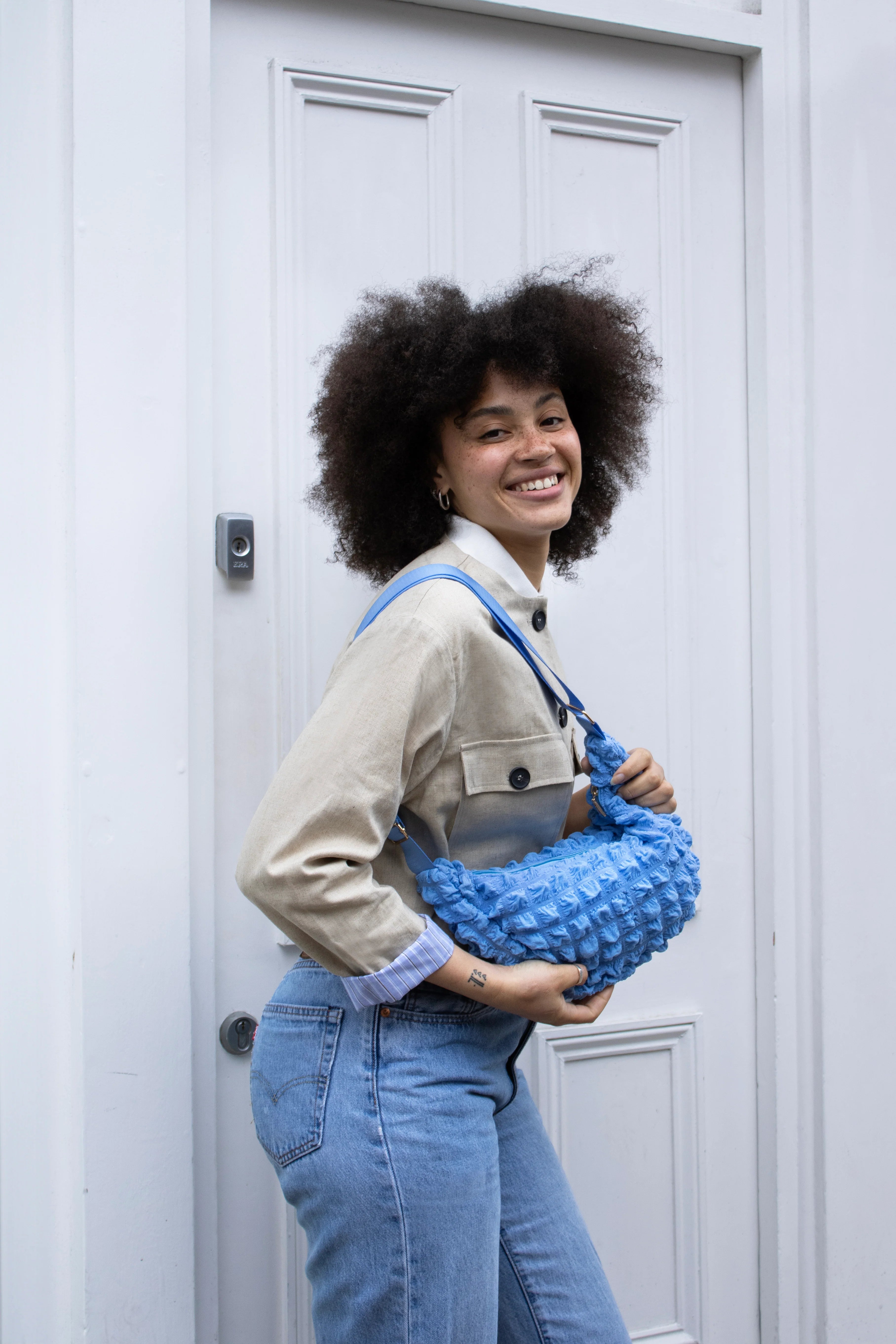 A light blue, textured, crescent-shaped crossbody bag held by a person.  The bag has a light blue strap.
