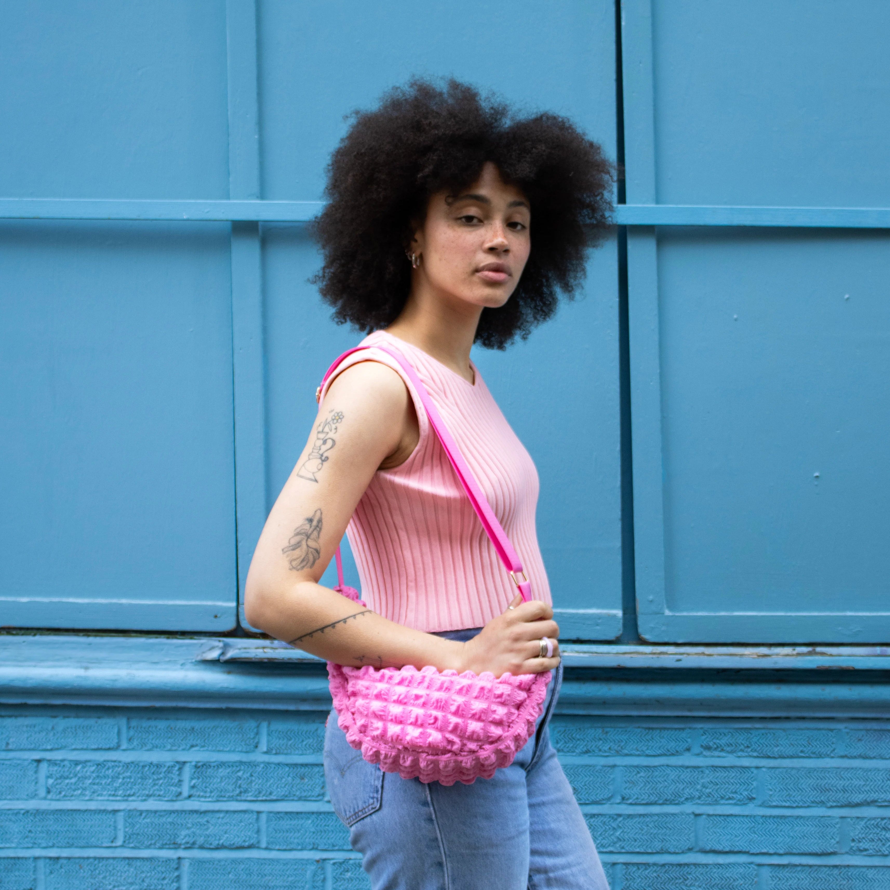 Pink textured crossbody bag with a ruffled design and bright pink strap.