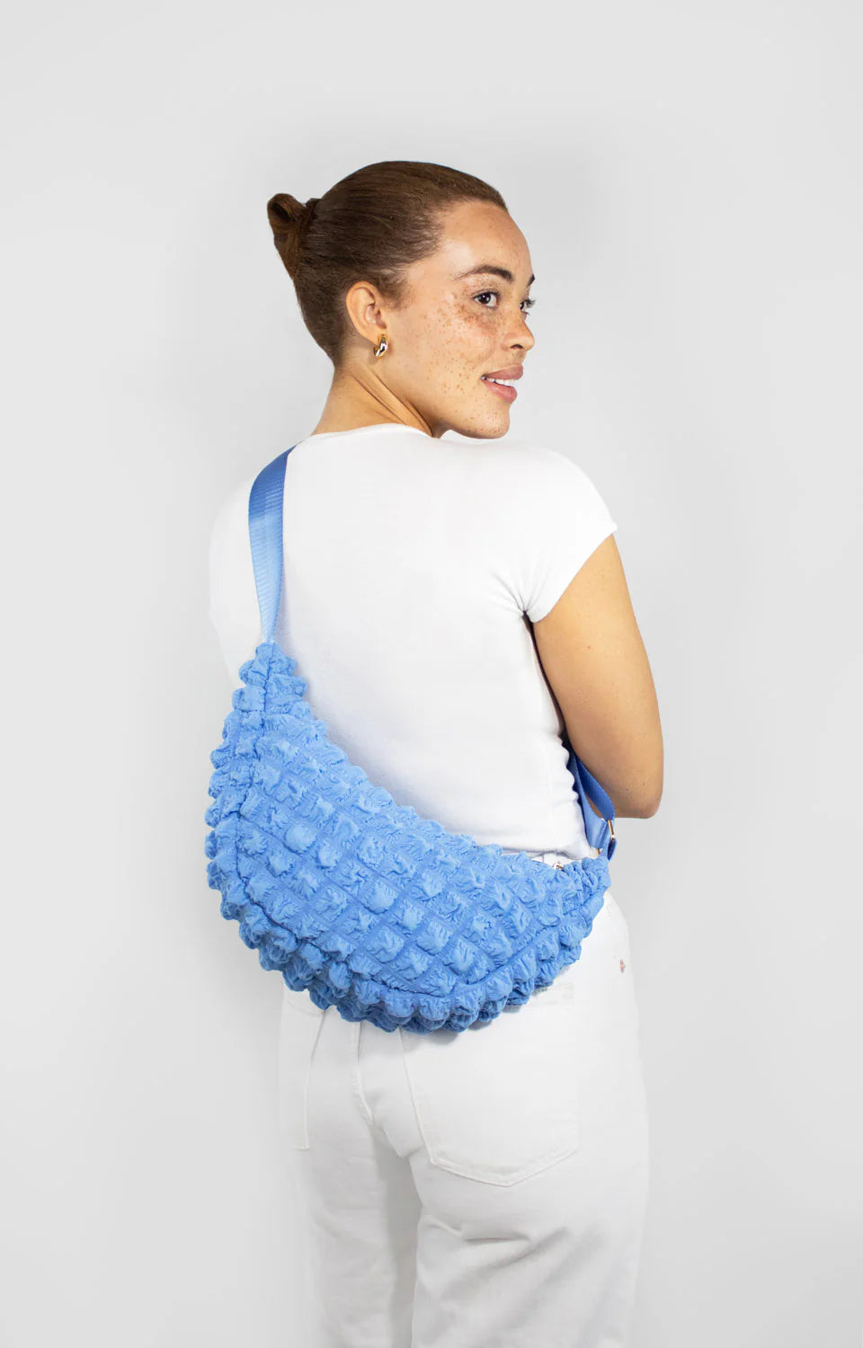 Powder blue textured crossbody bag with a curved shape and light blue strap.