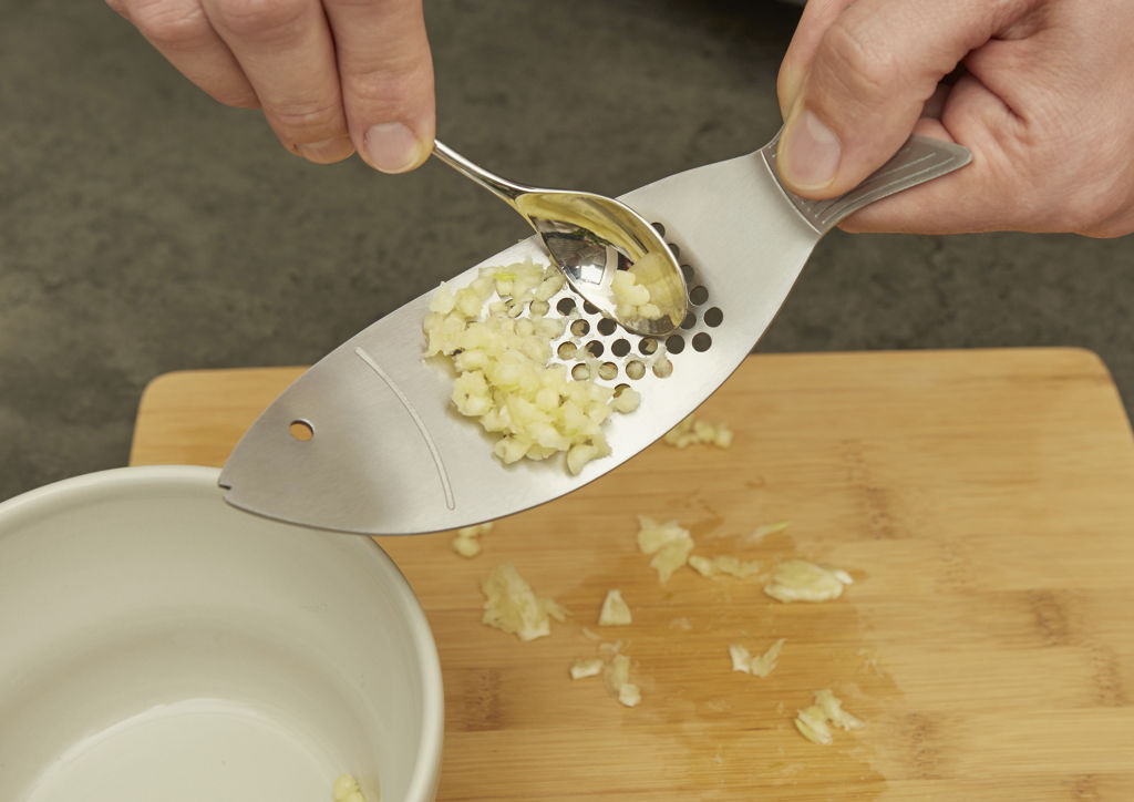 Minced garlic being scooped from a fish-shaped grater with a spoon.