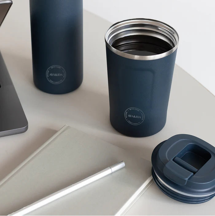 Blue insulated bottle and tumbler on a white surface with a blurred background