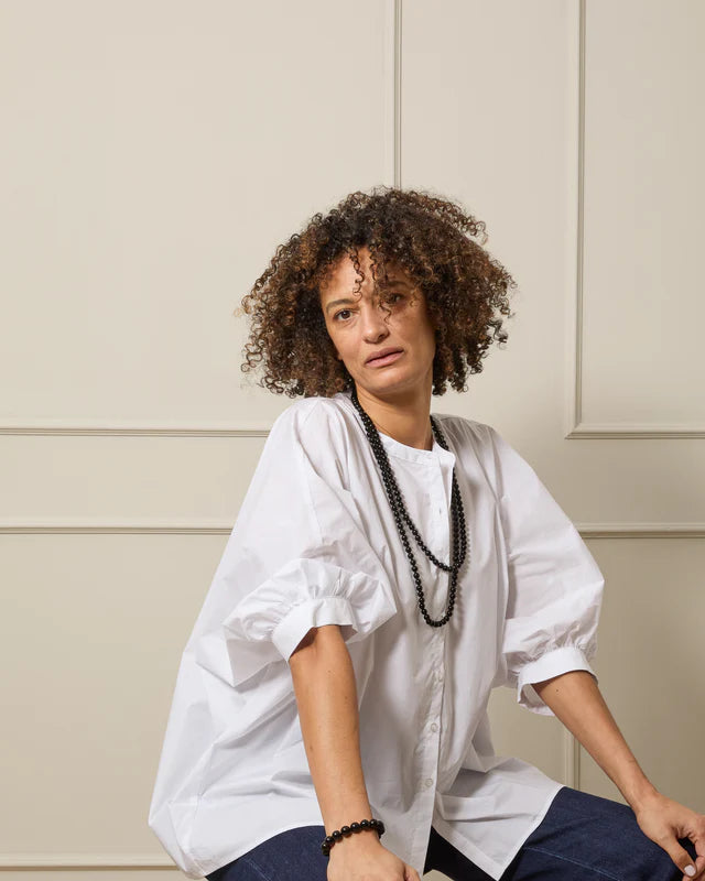 Woman wearing a white oversized blouse with balloon sleeves and a black beaded necklace.