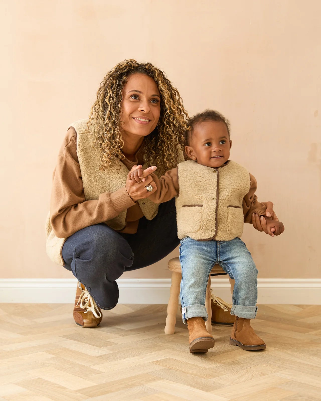 Woman and child in matching brown outfits sitting on a wooden floor.
