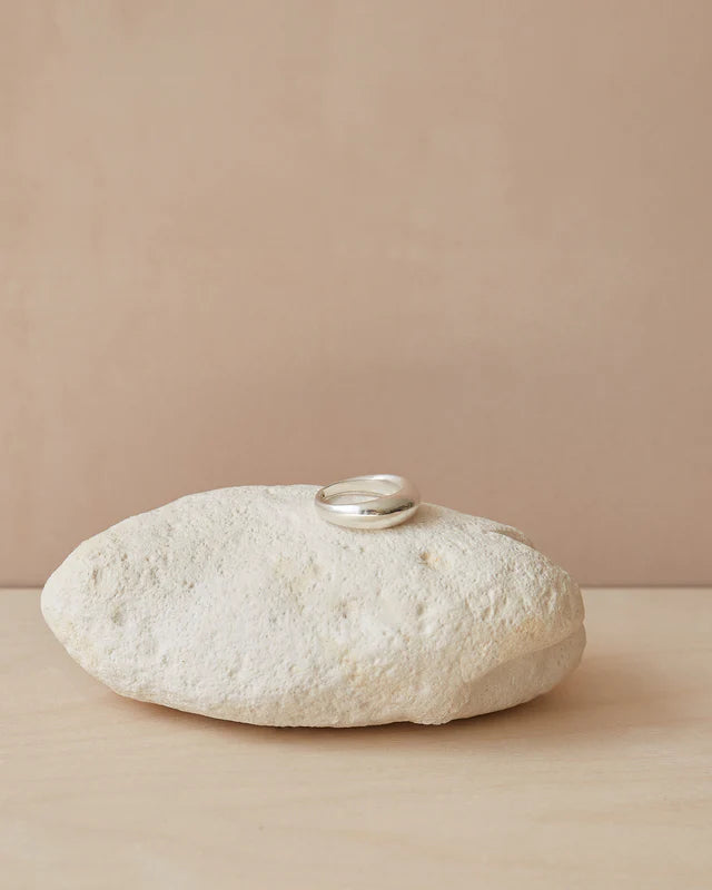 Silver dome ring resting on a light beige stone.