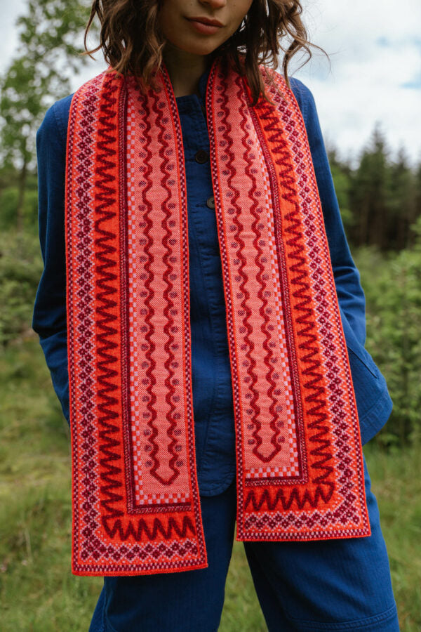 Long, coral-pink scarf with intricate embroidered red and burgundy geometric patterns.